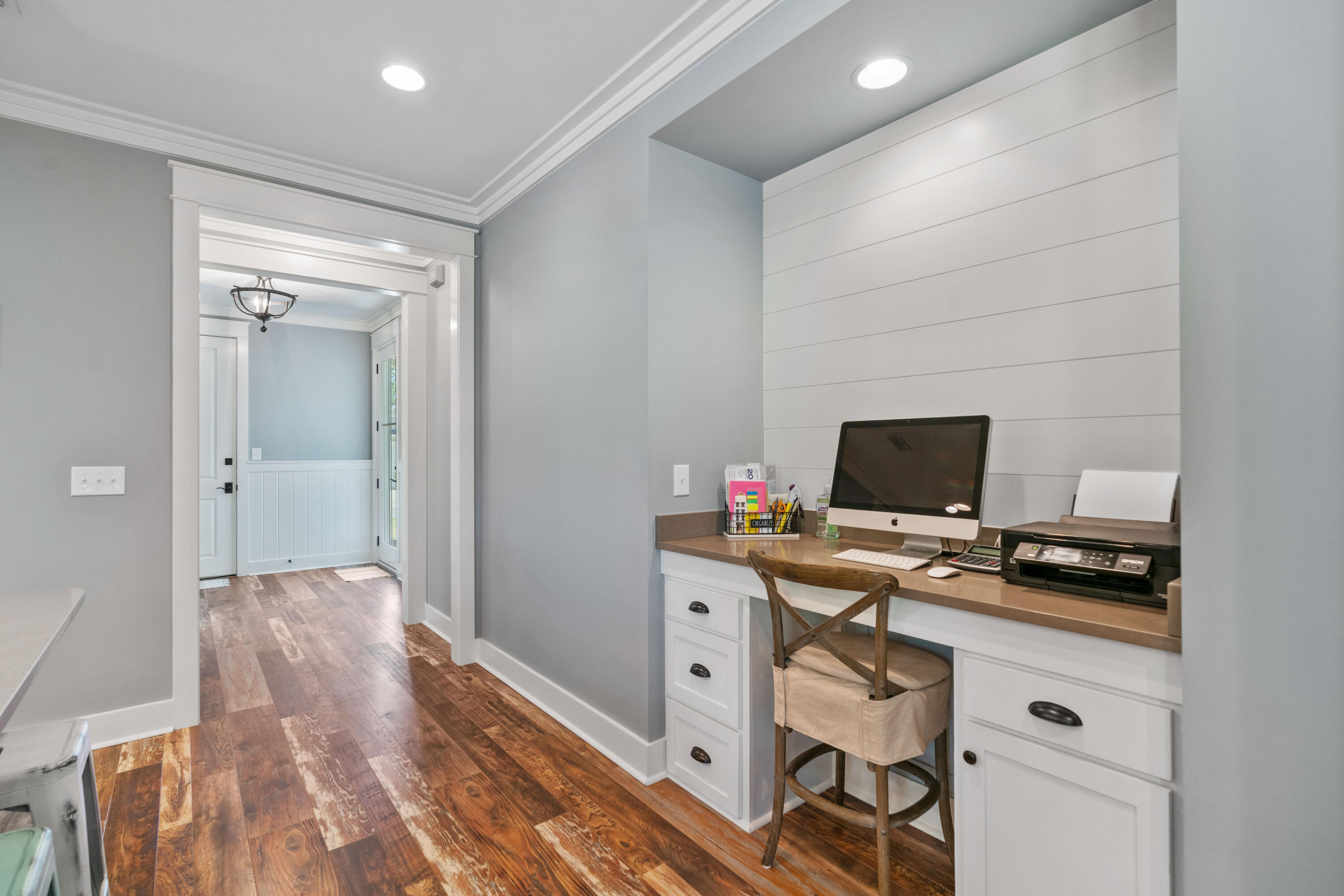 Home office with a built-in desk against a white shiplap wall and a doorway to the entry hall.