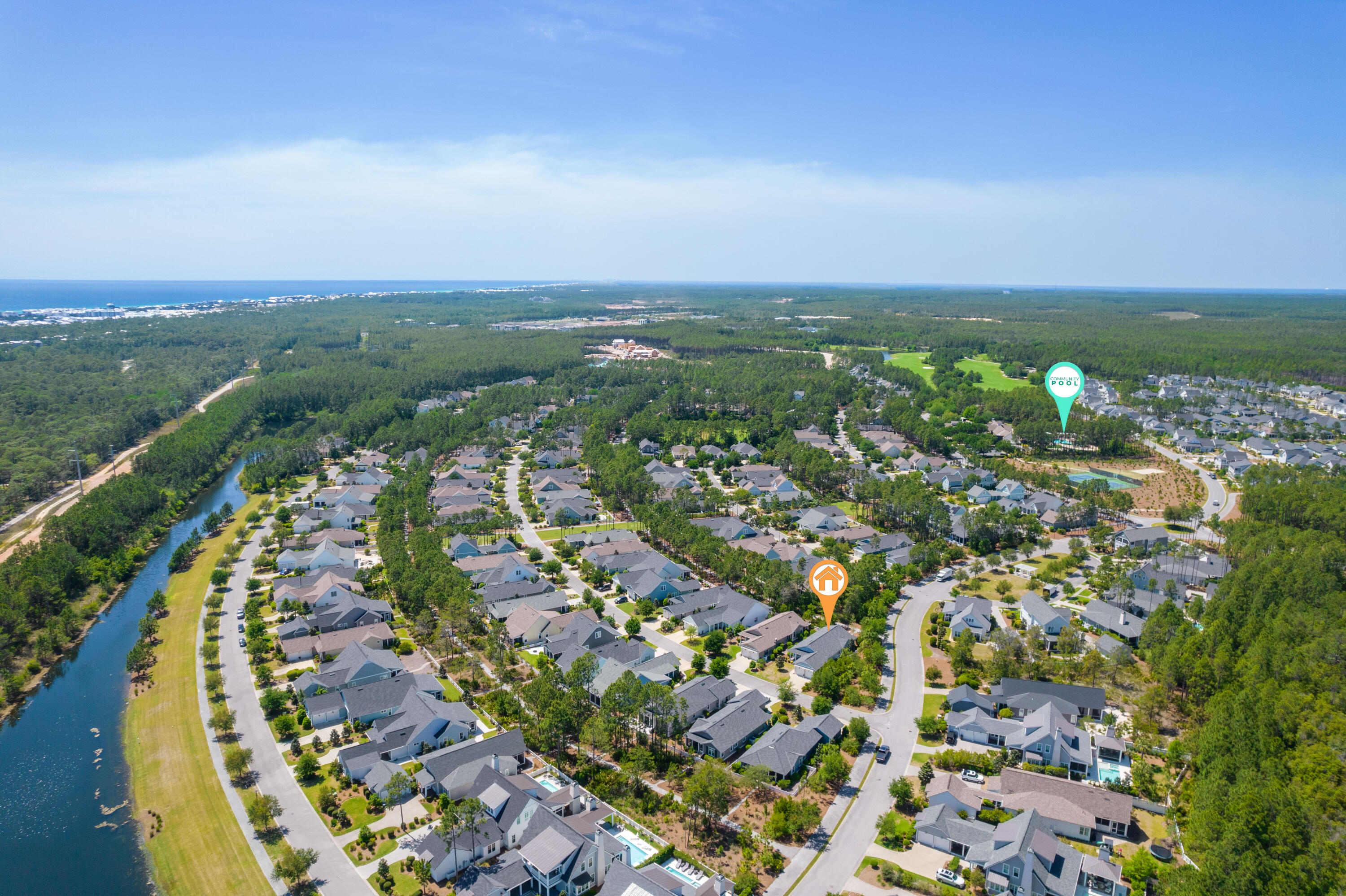Aerial view of a coastal neighborhood, with a canal, community pool marker, and ocean on the horizon.