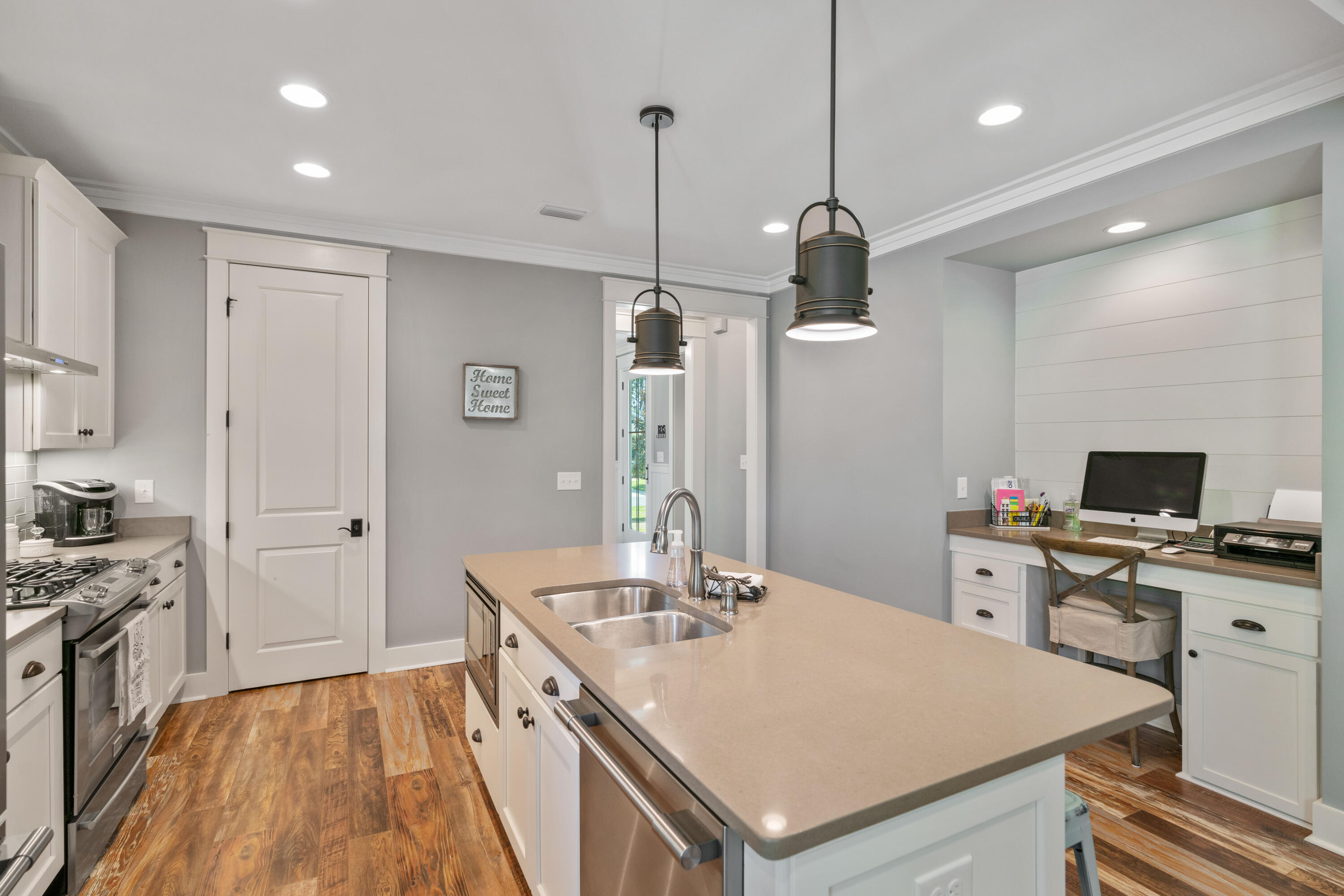Kitchen with a large sink island, white cabinetry, warm wood floors, and a built-in desk nook.