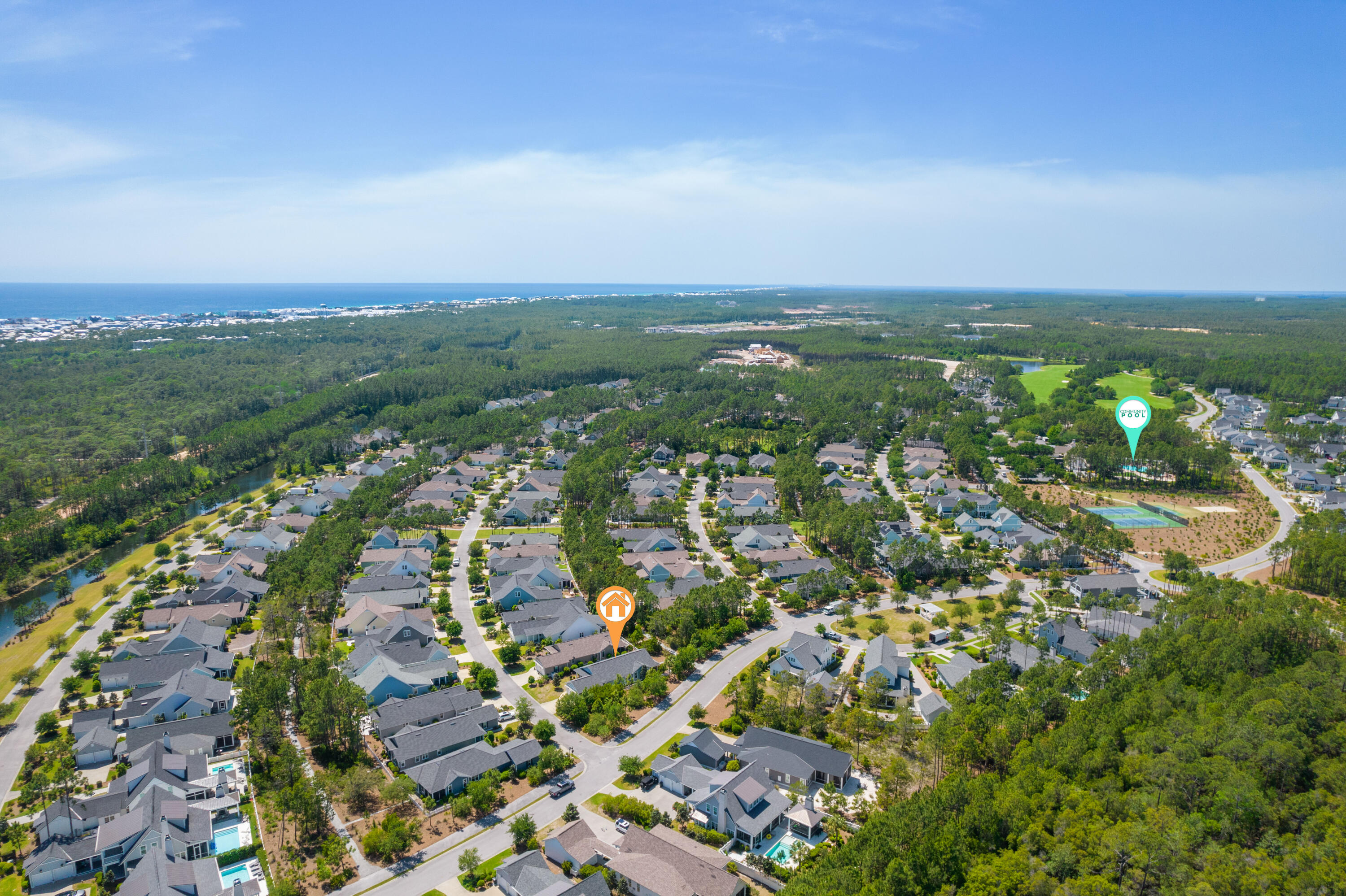 Aerial view of a wooded coastal neighborhood, with the home and community pool marked and the ocean on the horizon.