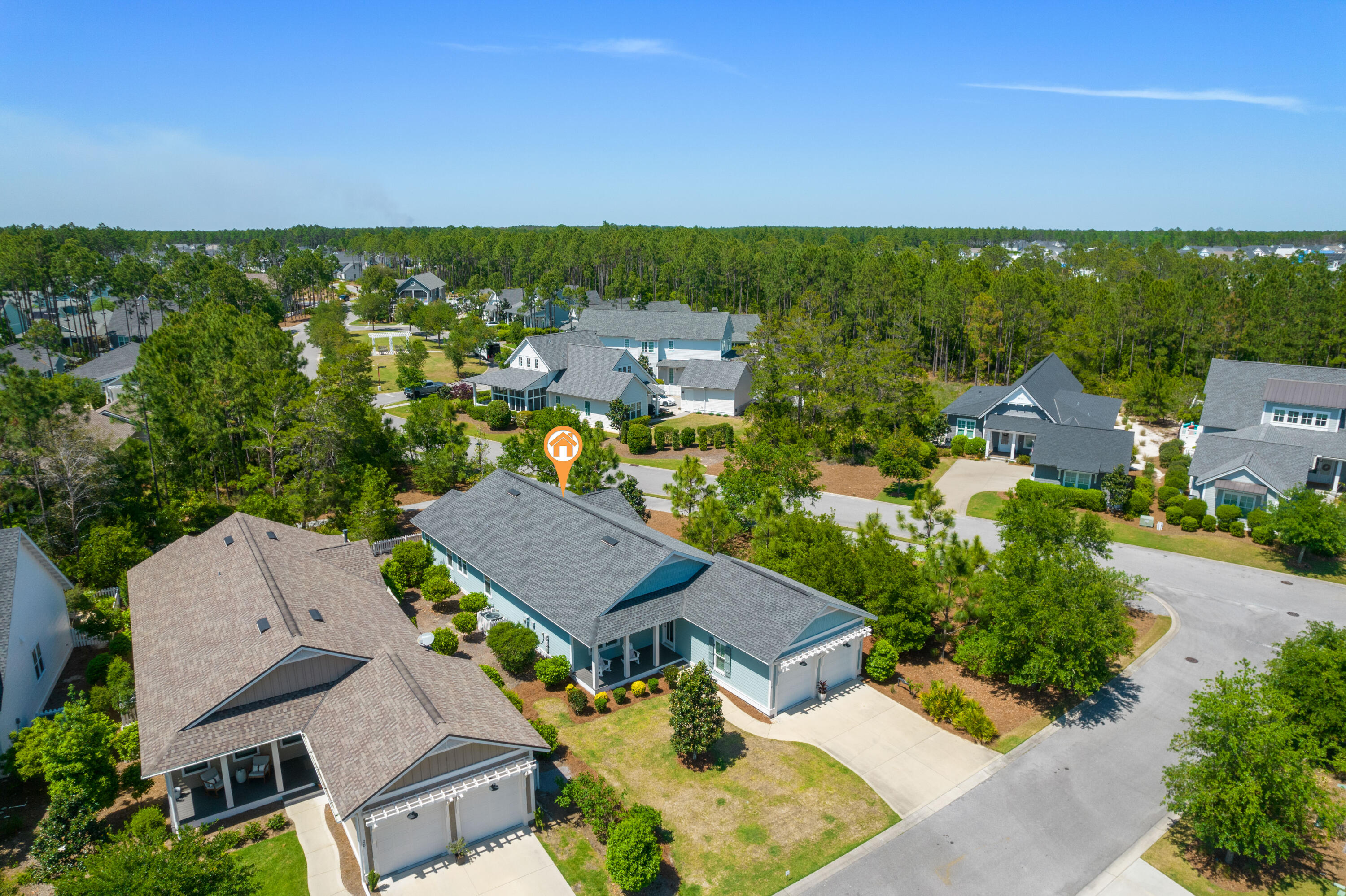 Aerial view of a teal home with a gray roof and landscaped yard among pine trees.