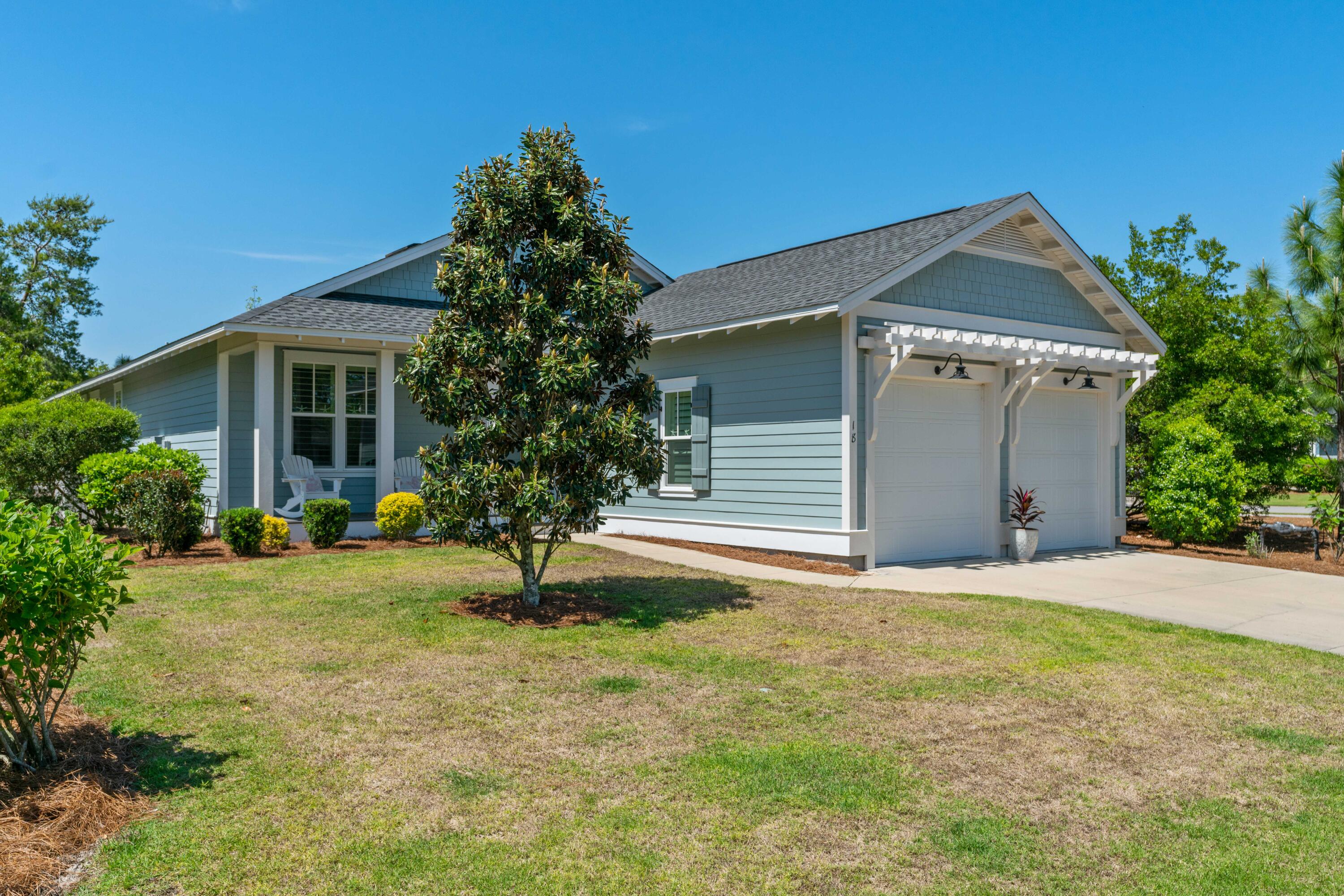 Light blue-gray home with a covered porch, double garage, and magnolia tree in the front yard.