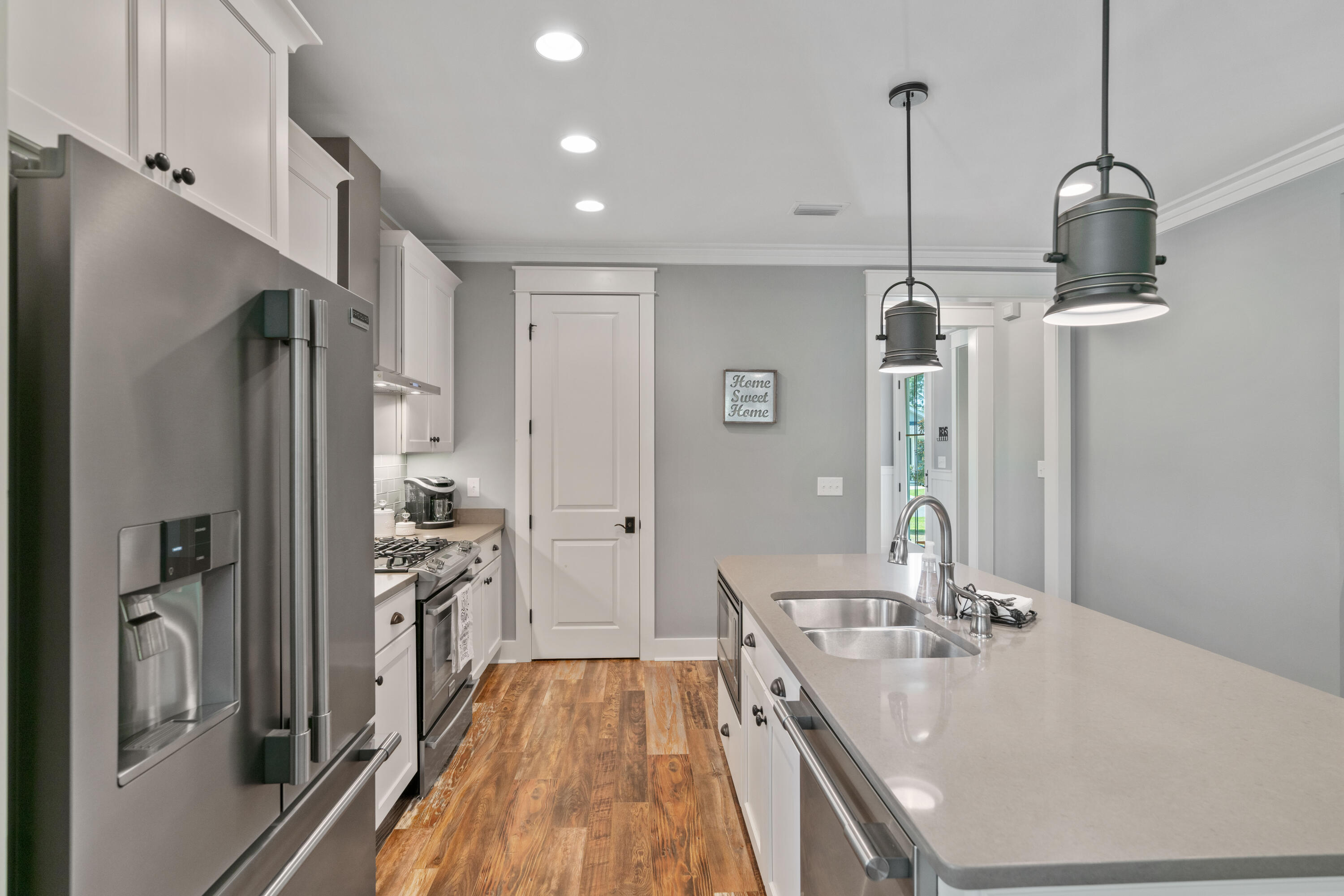 Kitchen with a large double-sink island, stainless steel appliances, white cabinets, and wood-look flooring.