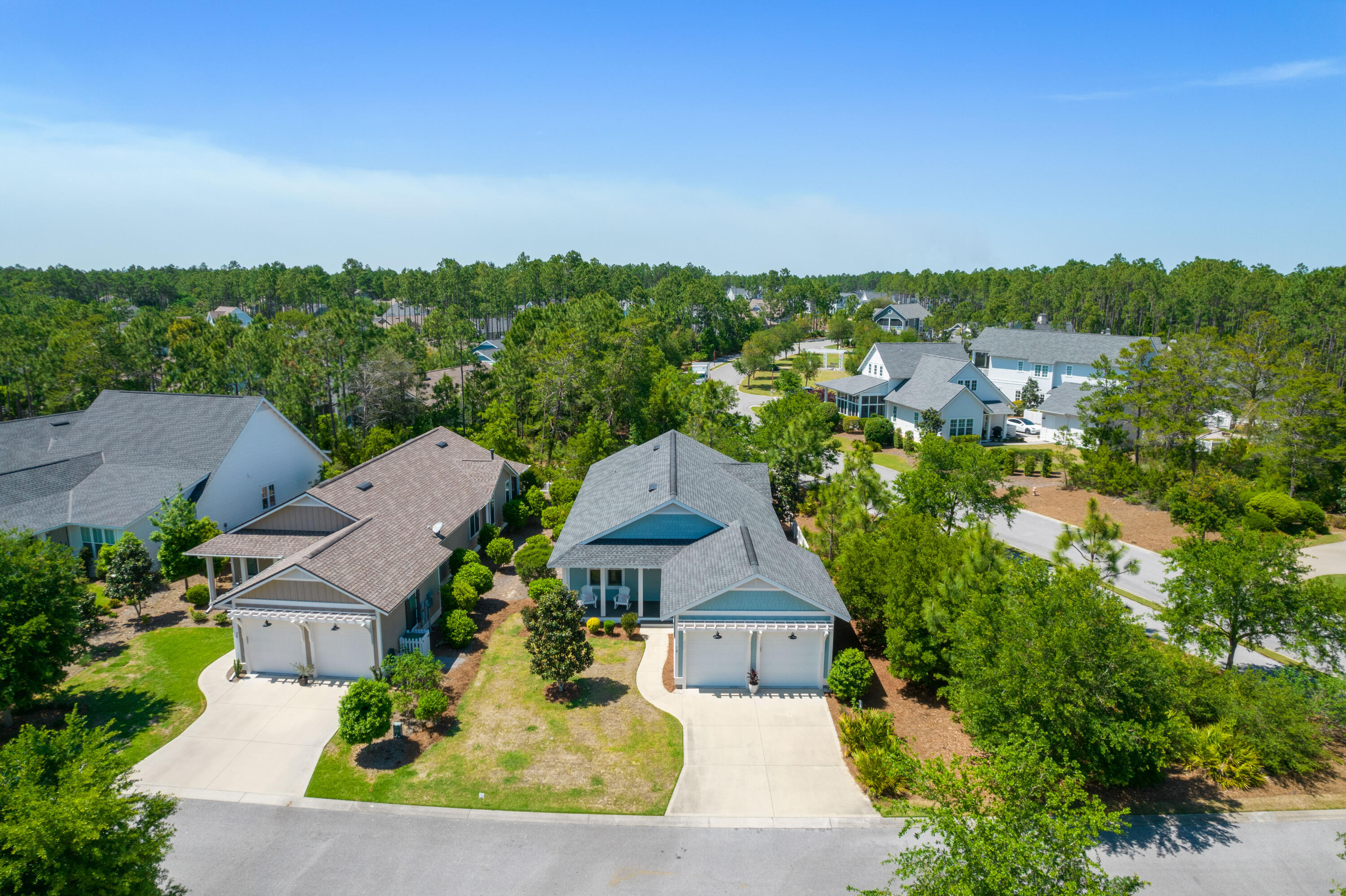Aerial view of a blue-gray home with a two-car garage, landscaped yard, and tree-lined neighborhood.