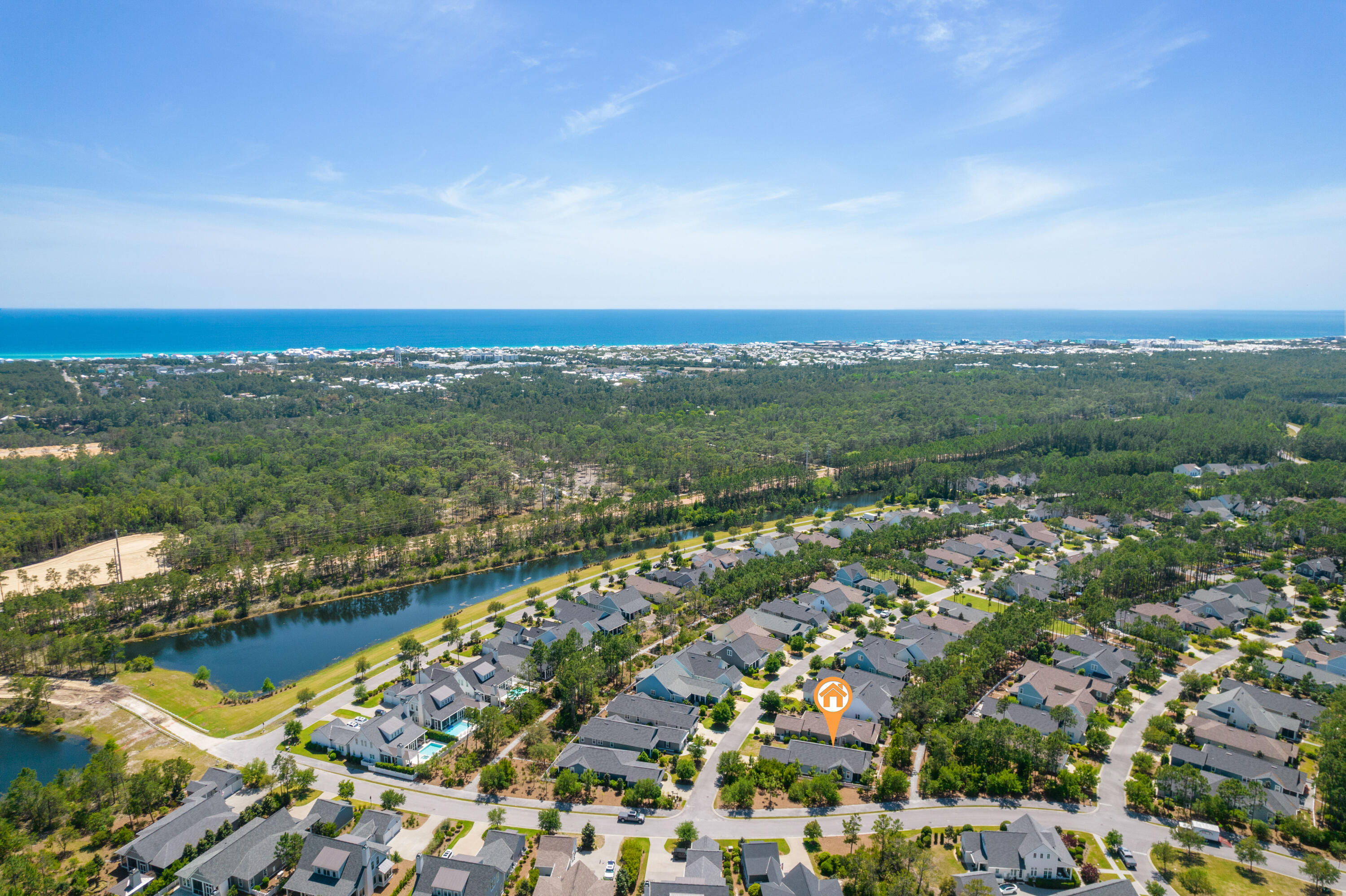 Aerial view of a coastal neighborhood, with a canal, wooded land, and the Gulf shoreline.