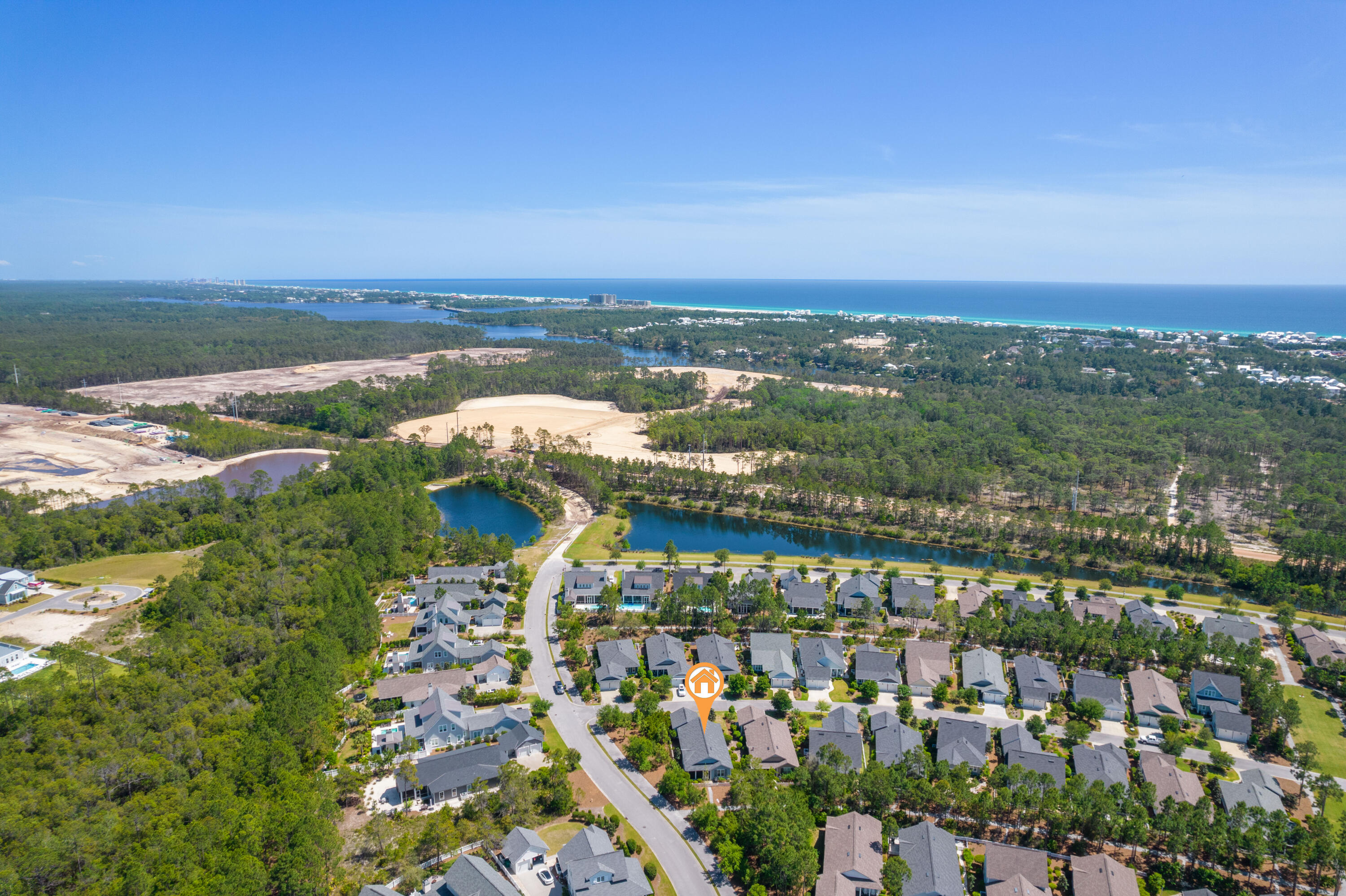 Aerial view of the home’s neighborhood, with wooded areas, ponds, and the Gulf shoreline beyond.