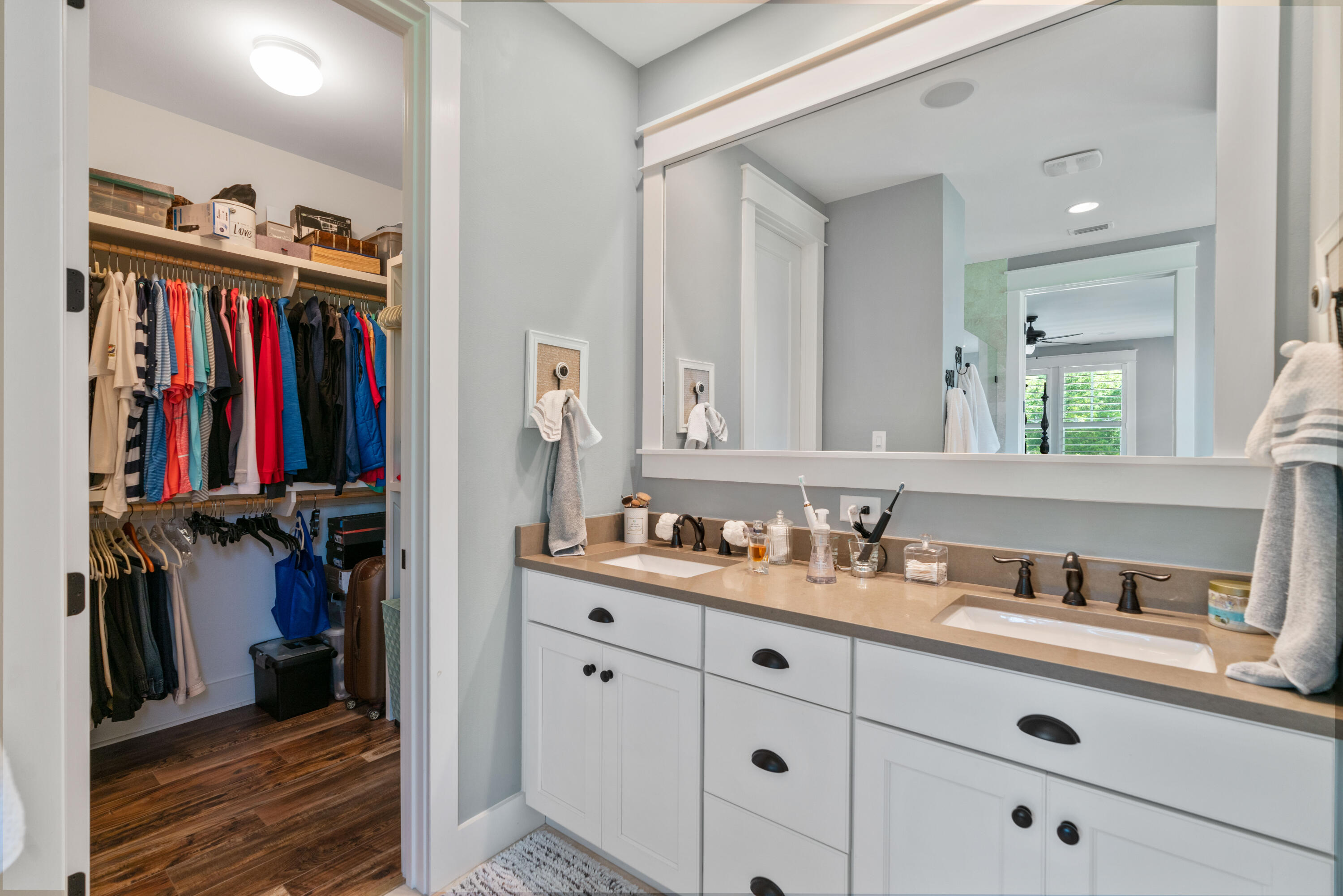 Bathroom with a white double-sink vanity and mirror beside an open walk-in closet.