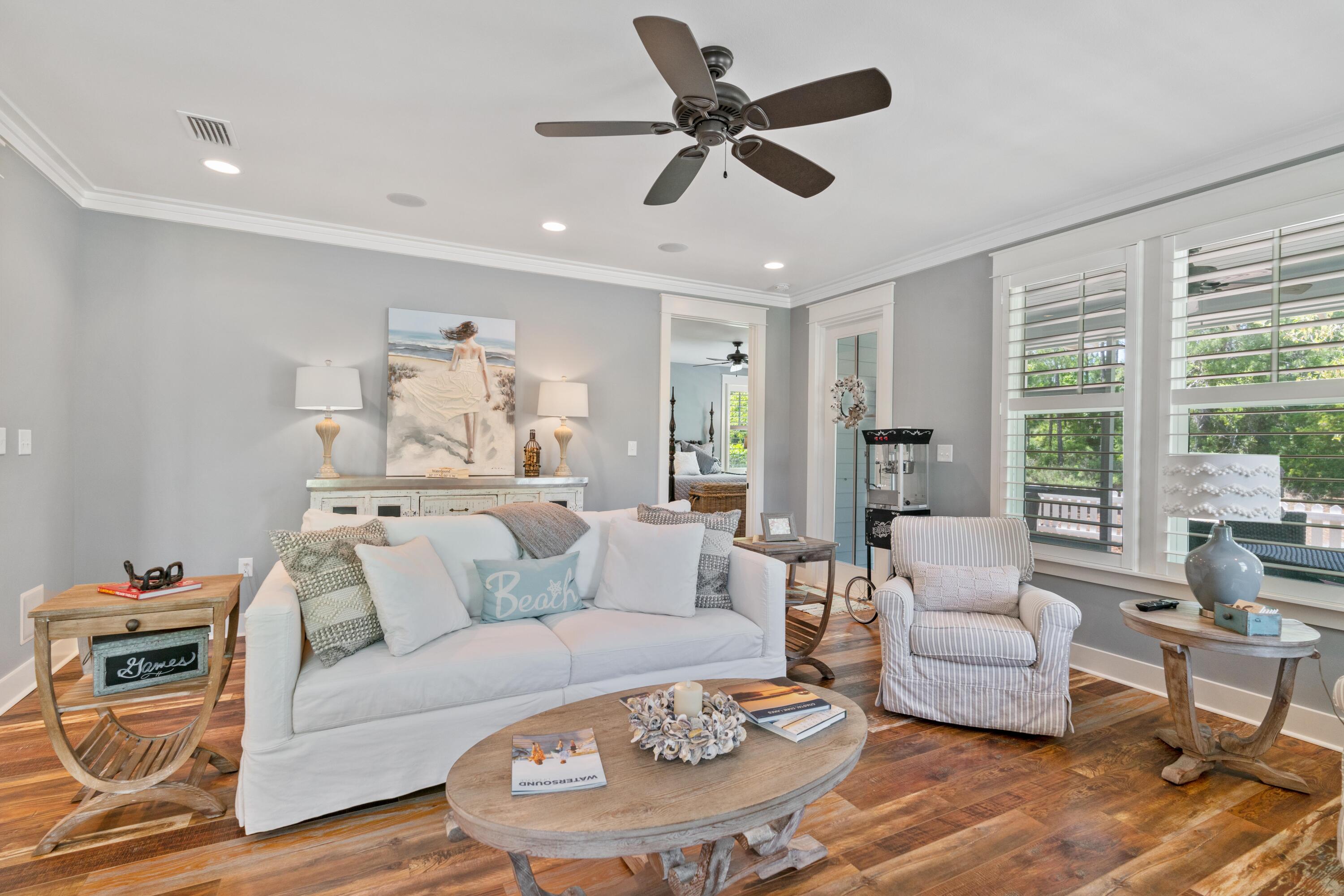 Living room with a white sofa, striped armchair, rustic wood tables, and plantation shutters.