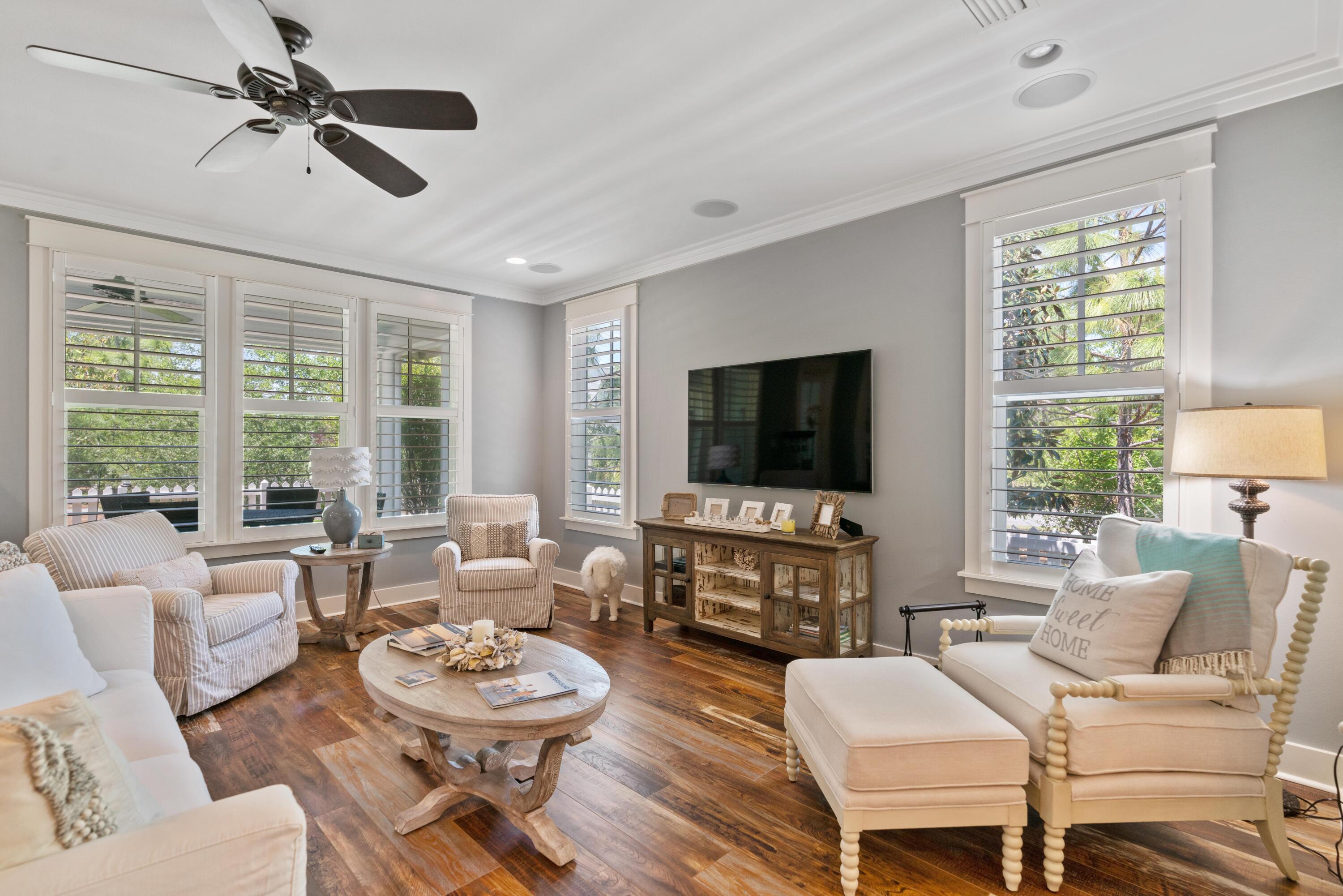 Furnished living room with plantation shutters, dark wood floors, and a wall-mounted television.