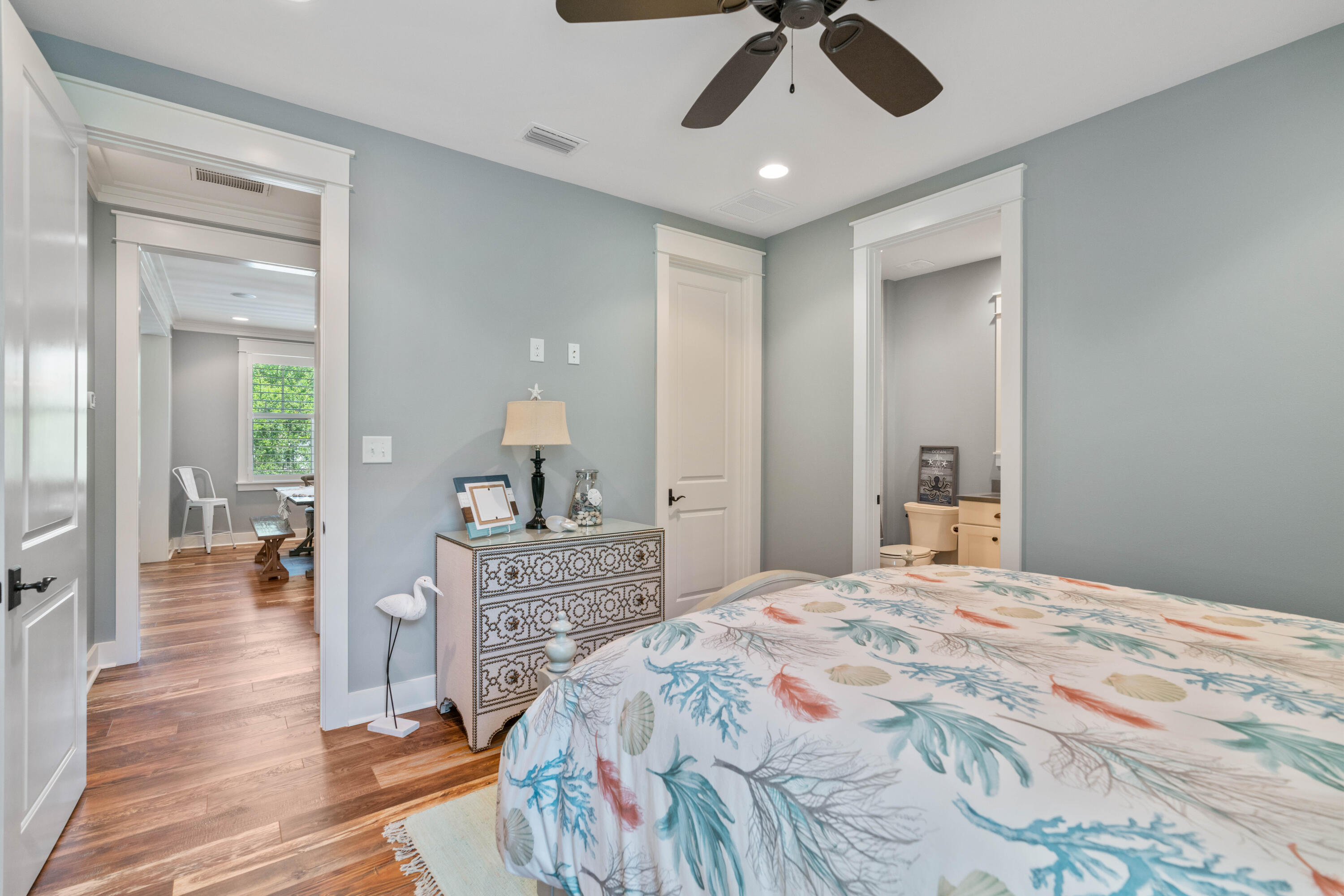 Bedroom with coastal-patterned bedding, a decorative dresser, and adjoining sitting area and bathroom.