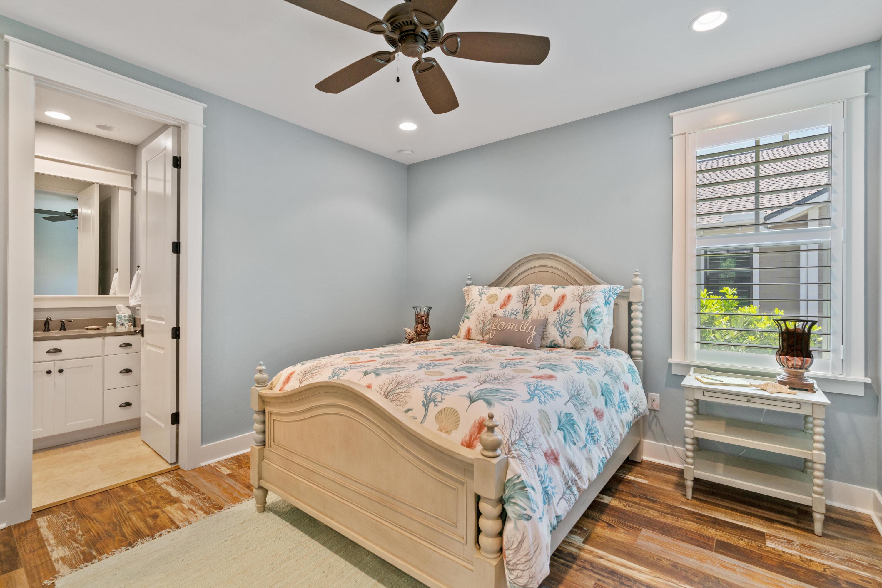 Bedroom with coastal-patterned bedding, a light wood bed, and an adjoining bathroom vanity.