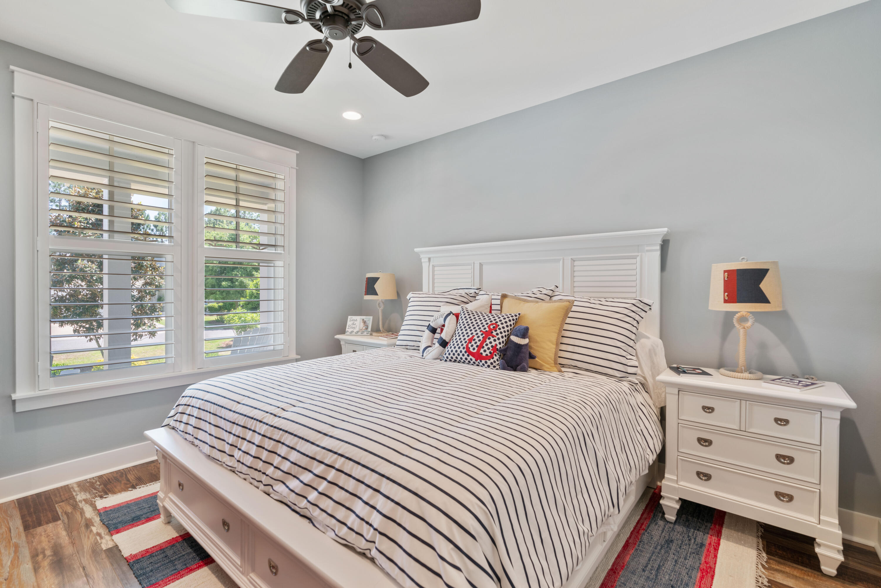Bedroom with navy-striped bedding, nautical accents, plantation shutters, and matching white furniture.