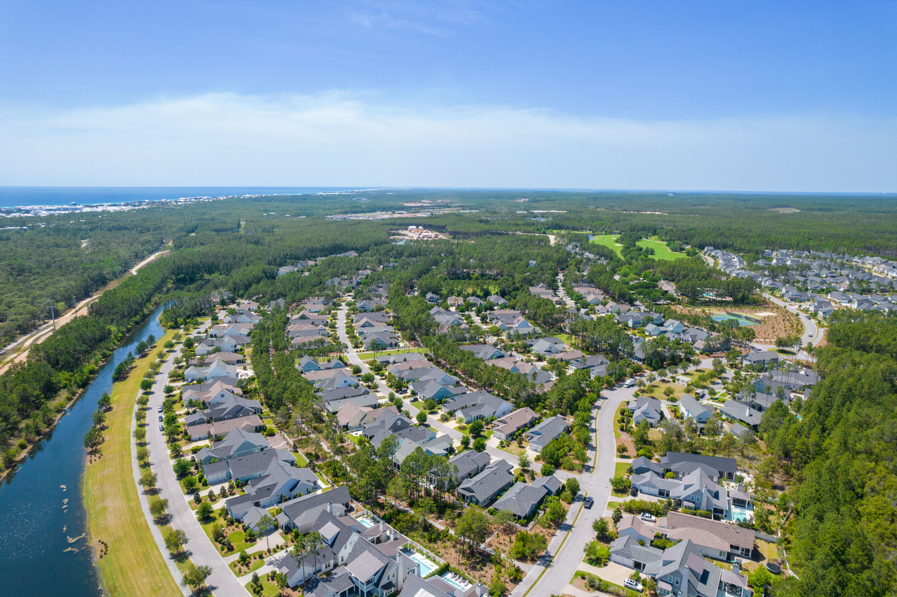 Aerial view of homes beside a canal, with a golf course and Gulf coastline in the distance.