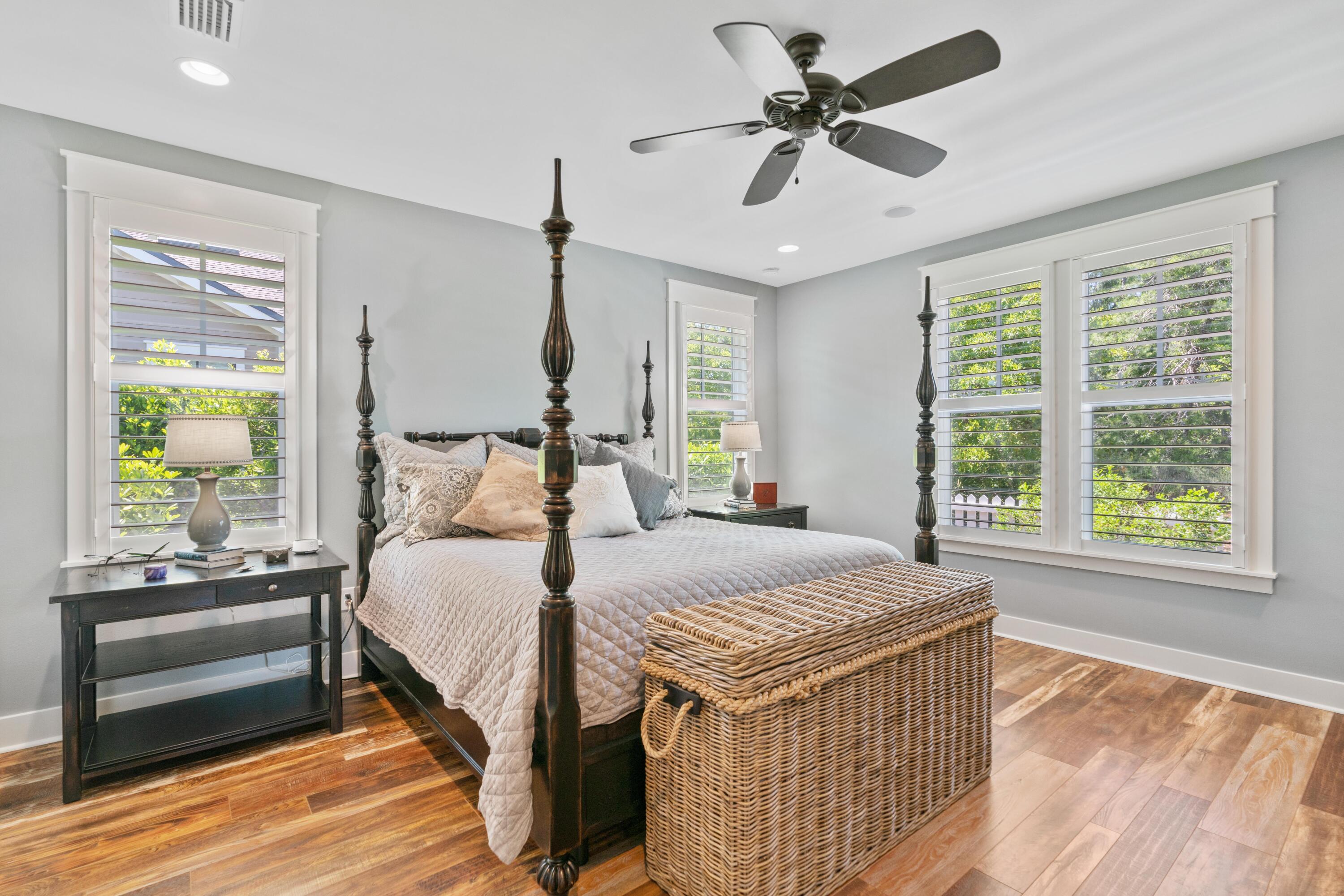 Bedroom with a dark four-poster bed, woven trunk, and bright shuttered windows.
