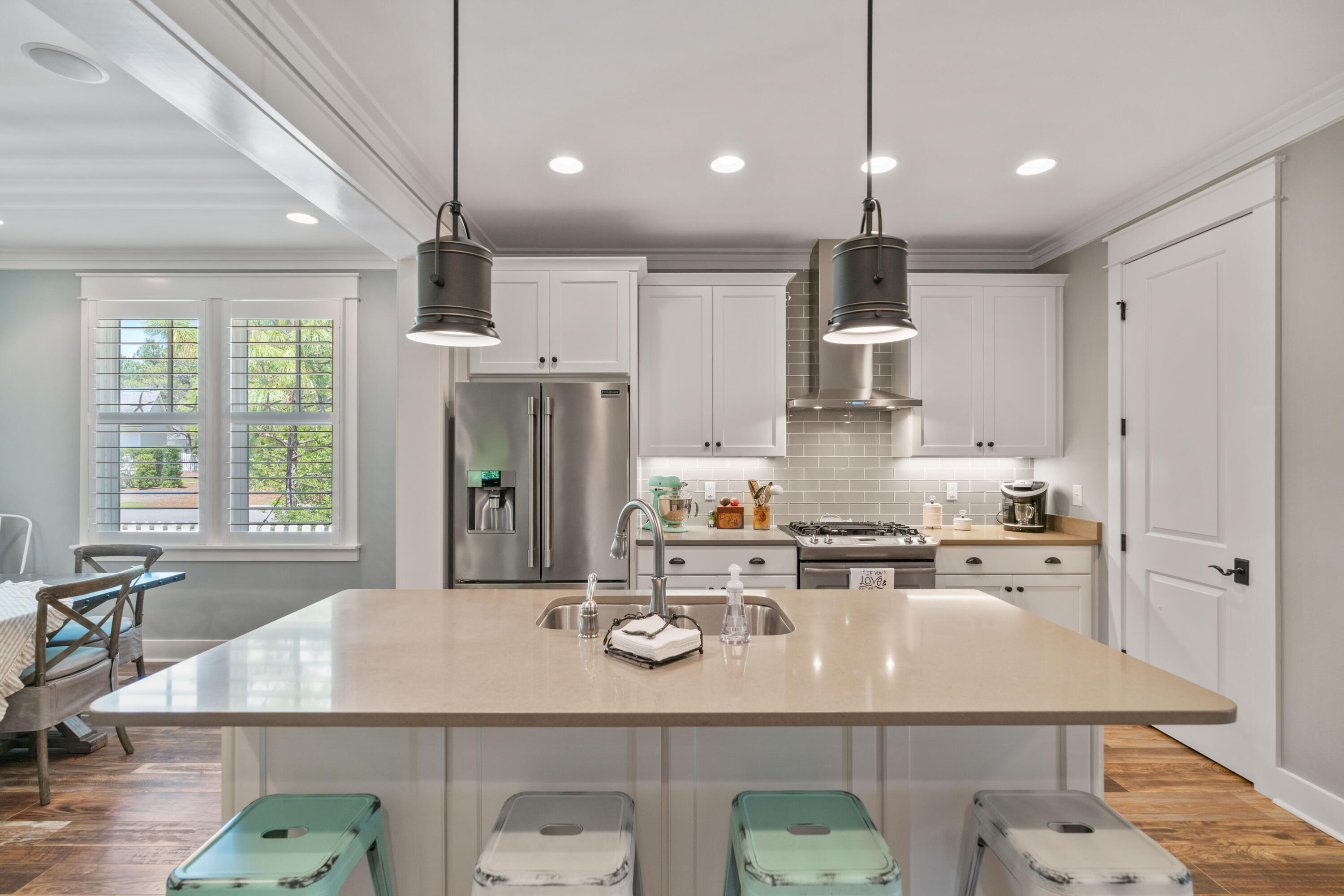 Kitchen with a large island, white cabinetry, stainless steel appliances, and shuttered windows overlooking greenery.