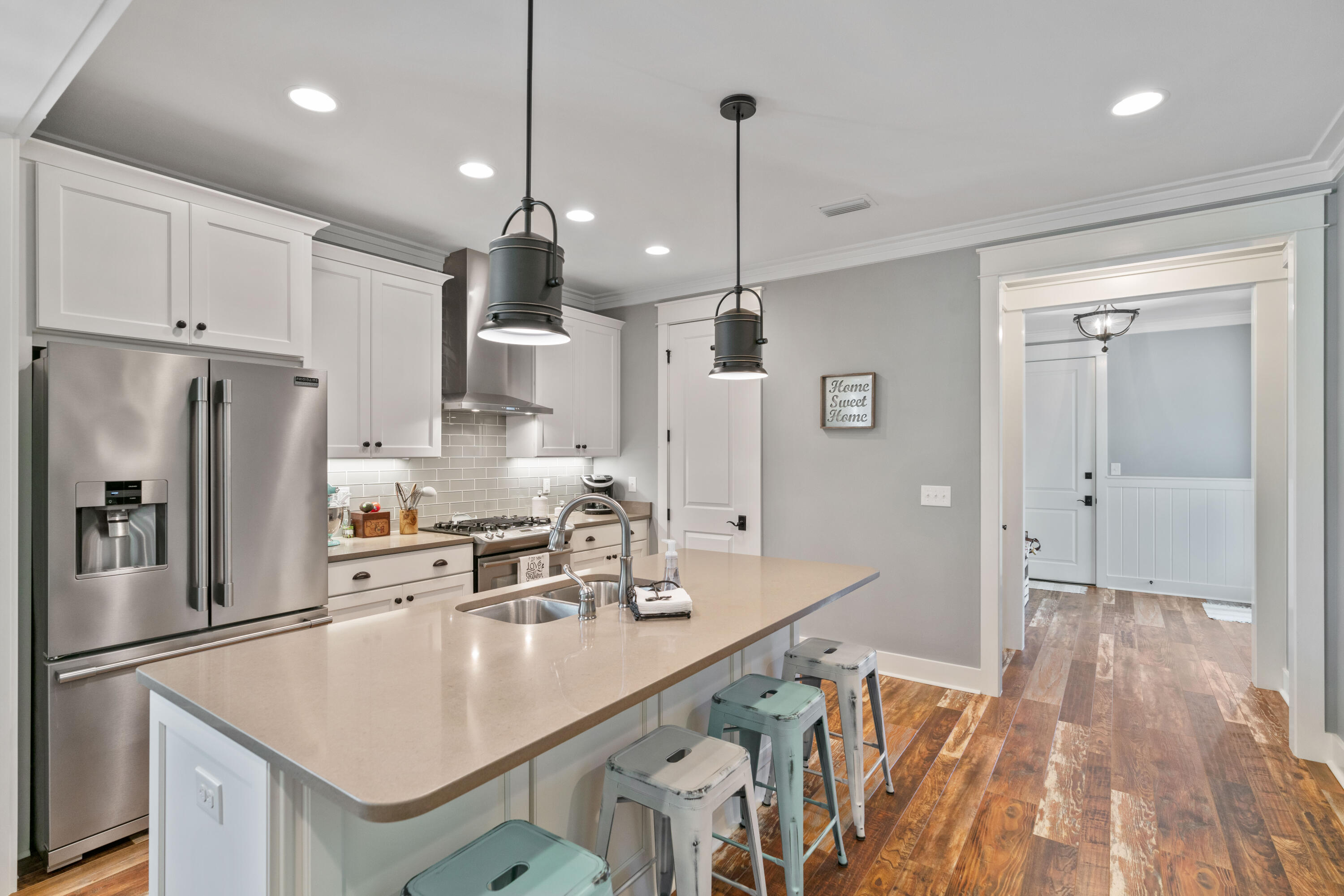 Kitchen with a large island, stainless steel appliances, white cabinets, and wood-look floors.