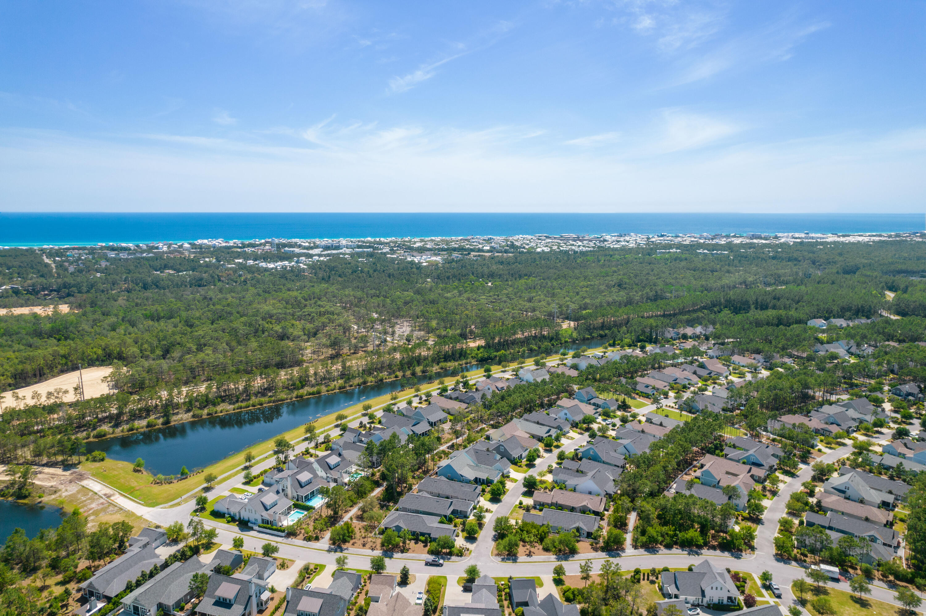 Aerial view of a coastal neighborhood beside a canal, with forest and ocean beyond.