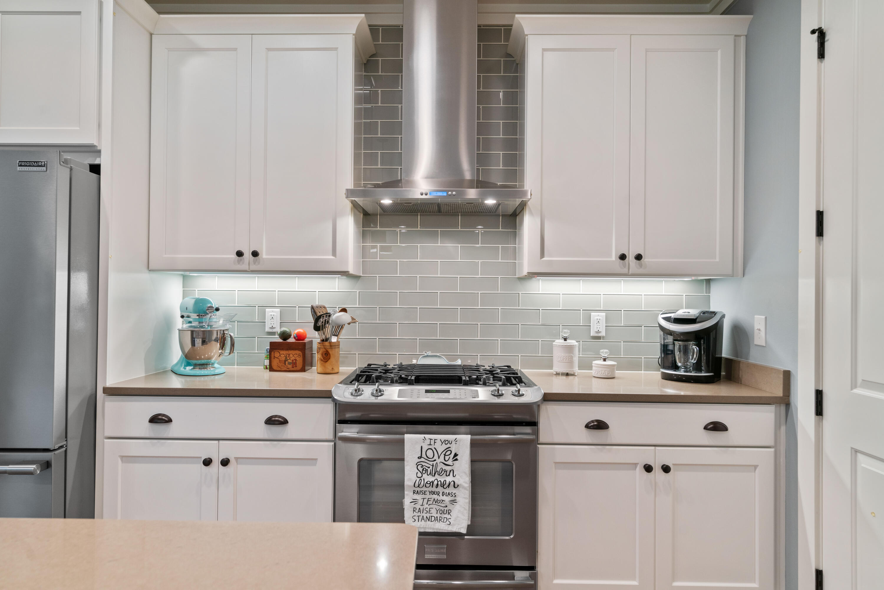 Kitchen with white cabinetry, gray tile backsplash, stainless range, and turquoise stand mixer.