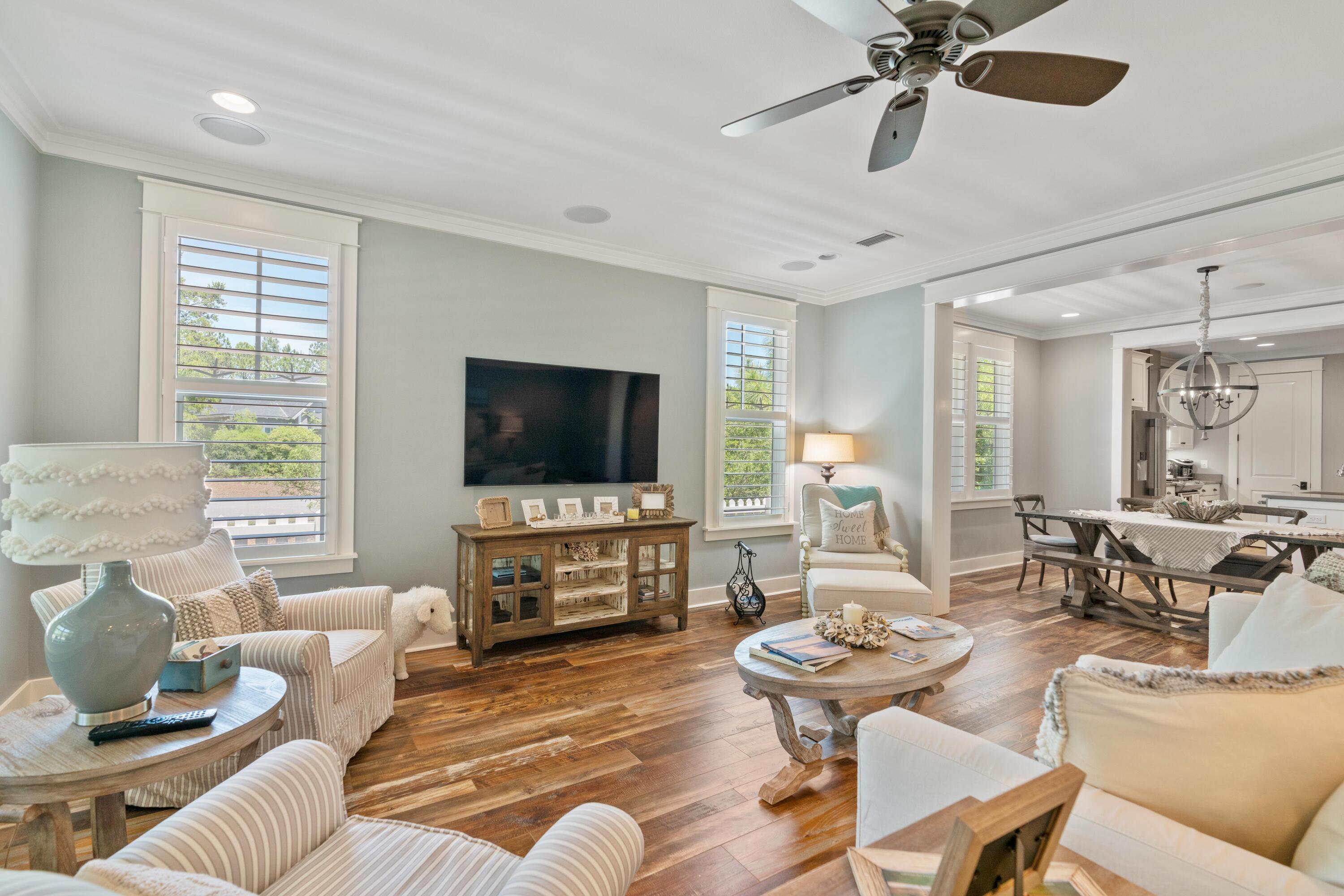 Furnished living room with wood floors, plantation shutters, and an adjoining dining area.