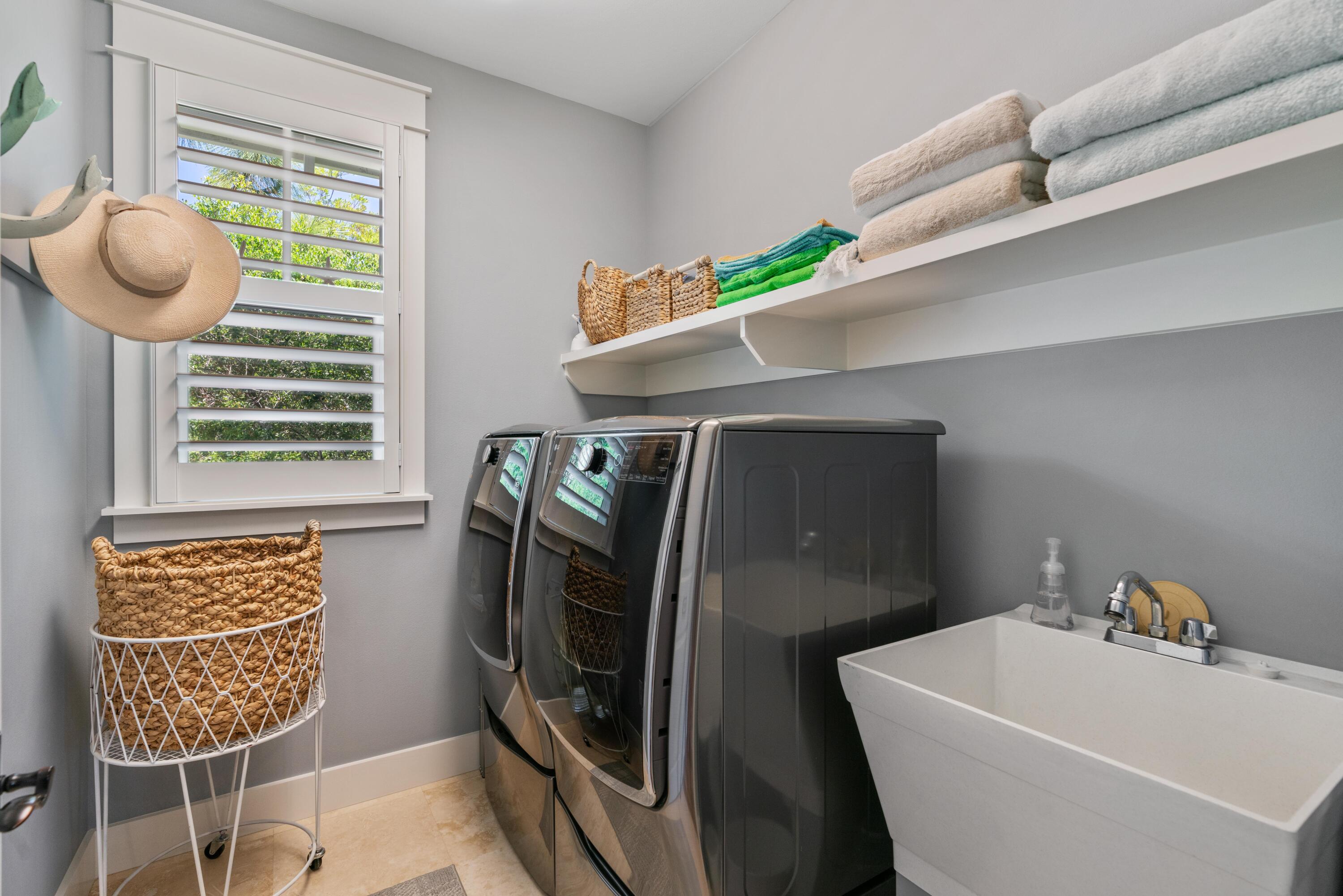 Laundry room with front-loading washer and dryer, deep utility sink, and shelves of folded towels.