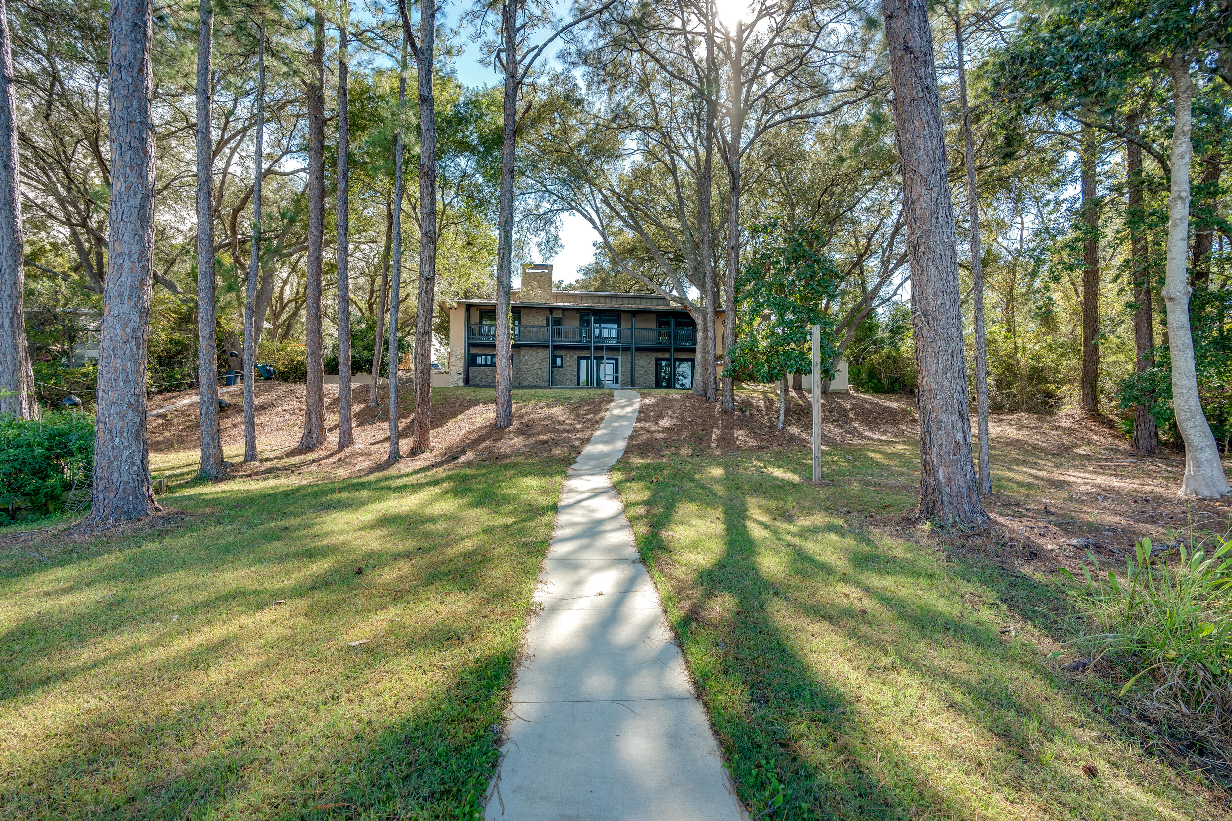 Two-story house among mature trees, approached by a concrete walkway, with a covered upper balcony.