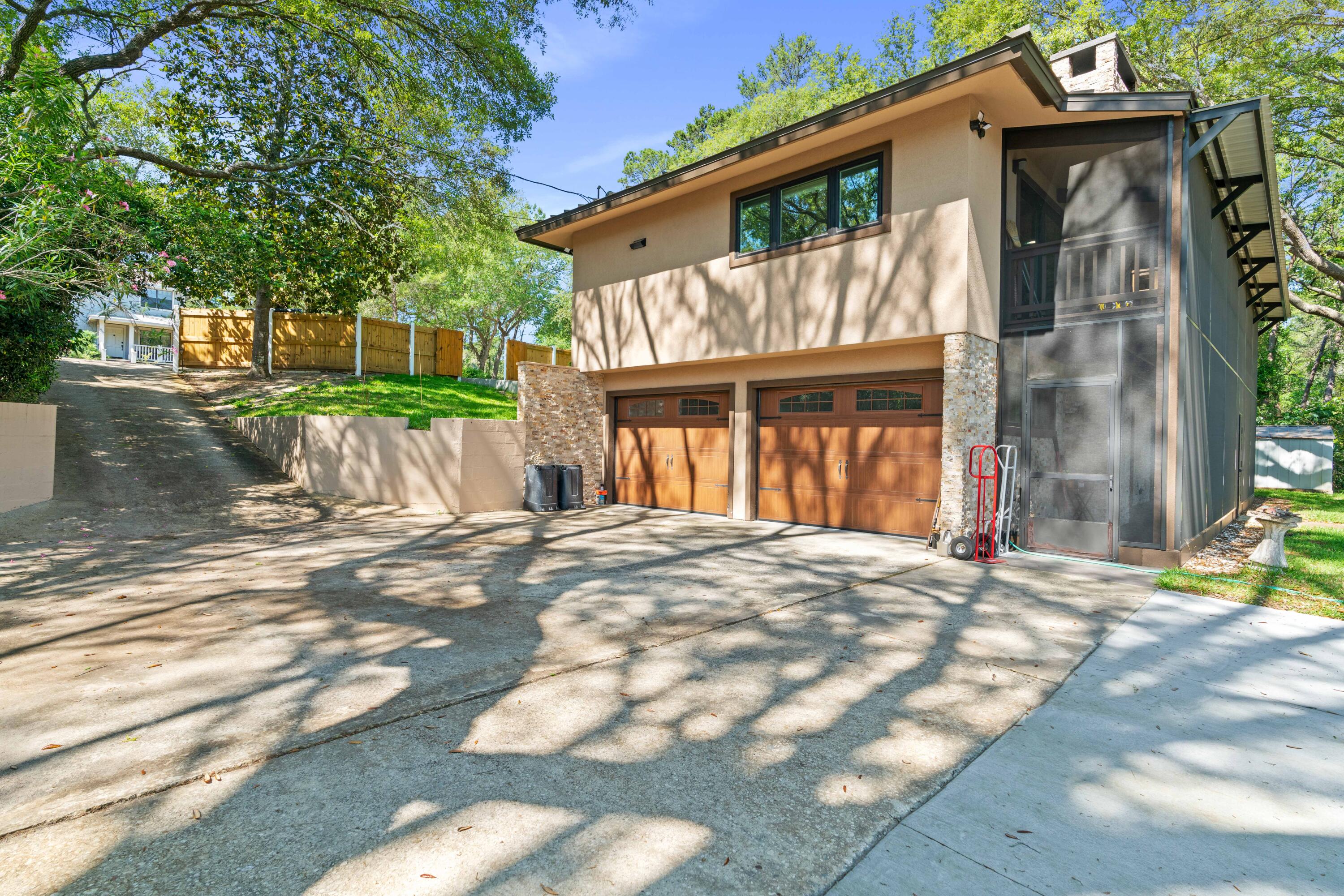 Modern tan home with two wooden garage doors, stone accents, and a screened side enclosure.