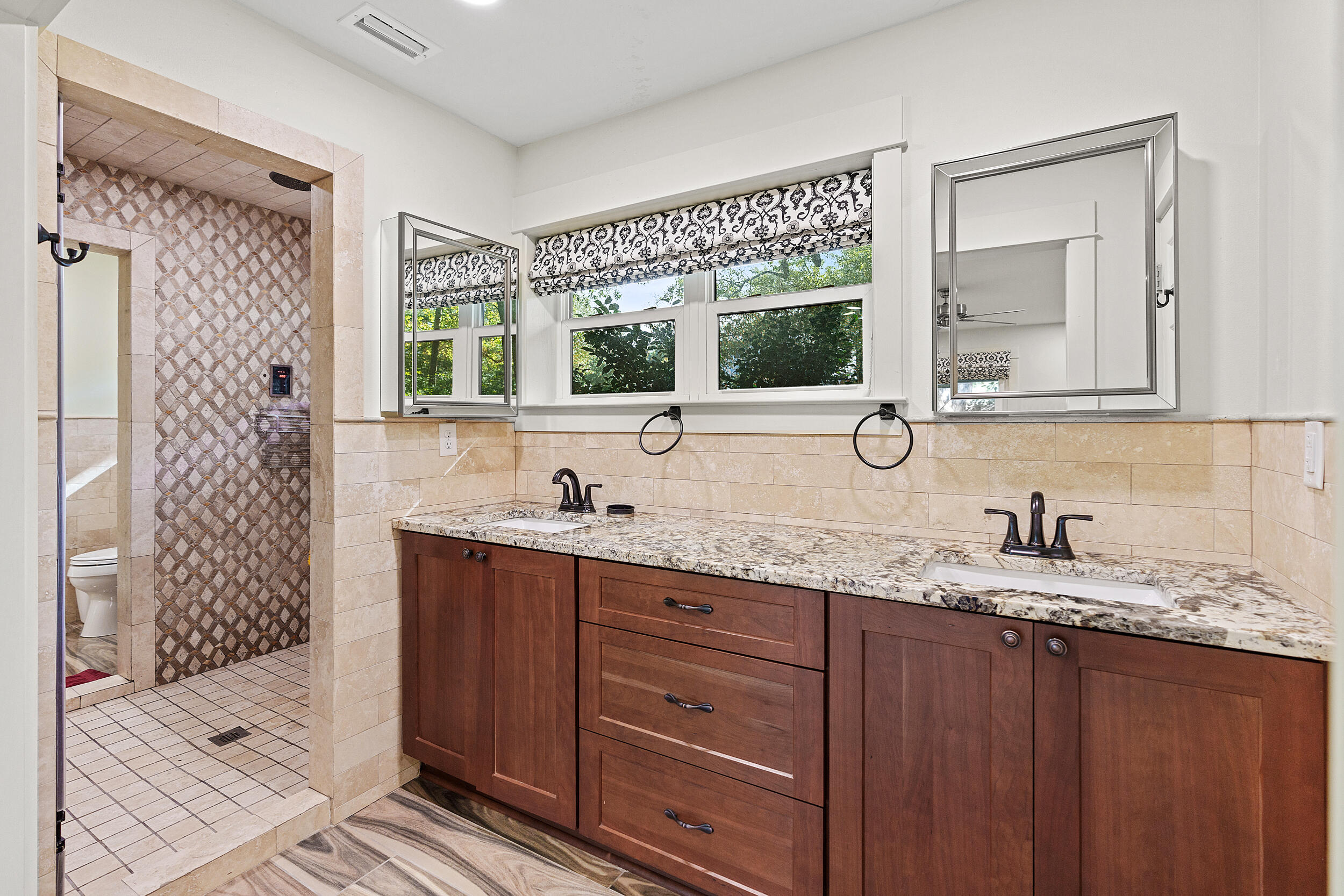 Bathroom with a double-sink wood vanity and a tiled walk-in shower with a patterned accent wall.