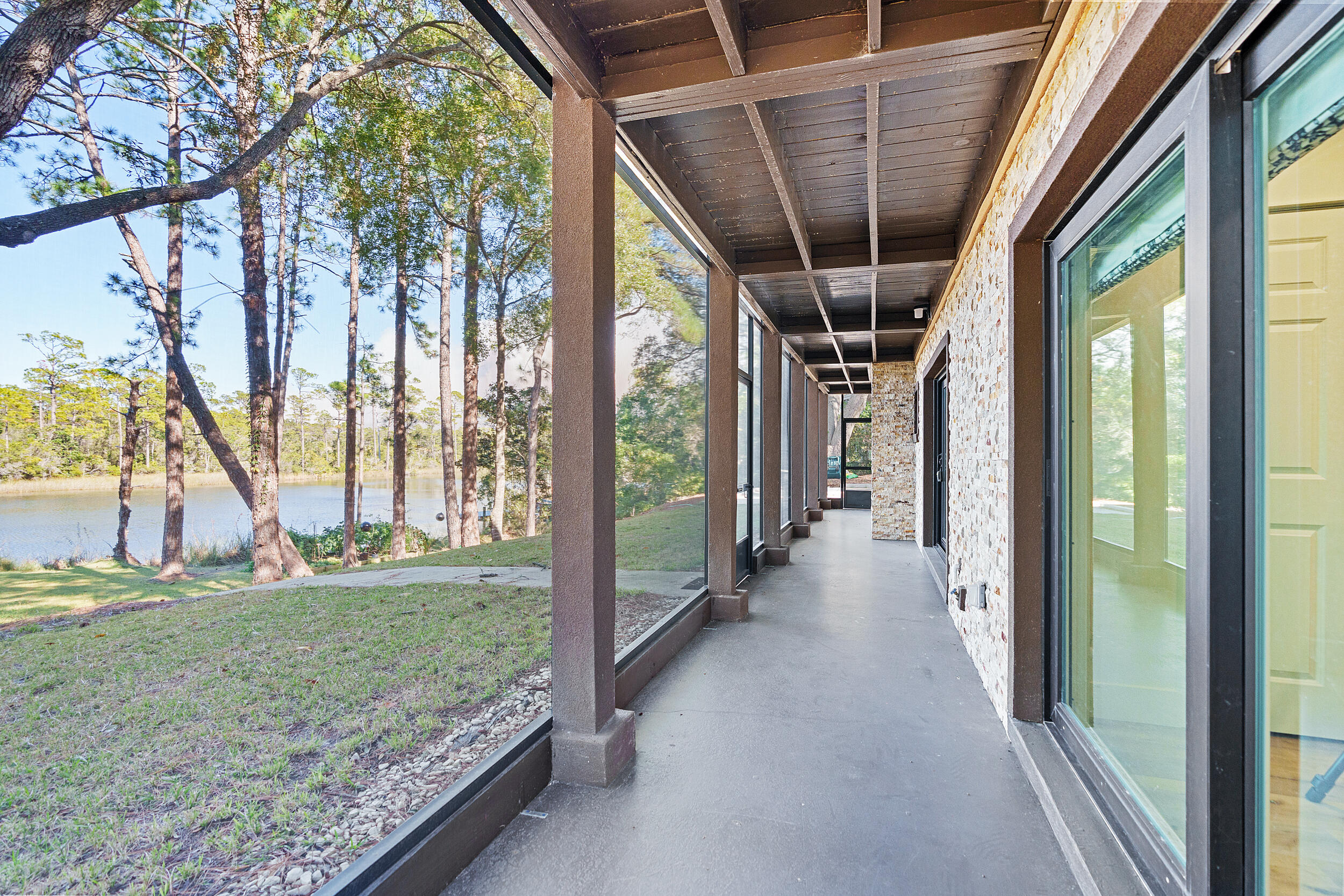 Covered lakeside porch with stone wall, large windows, and a tree-lined water view.