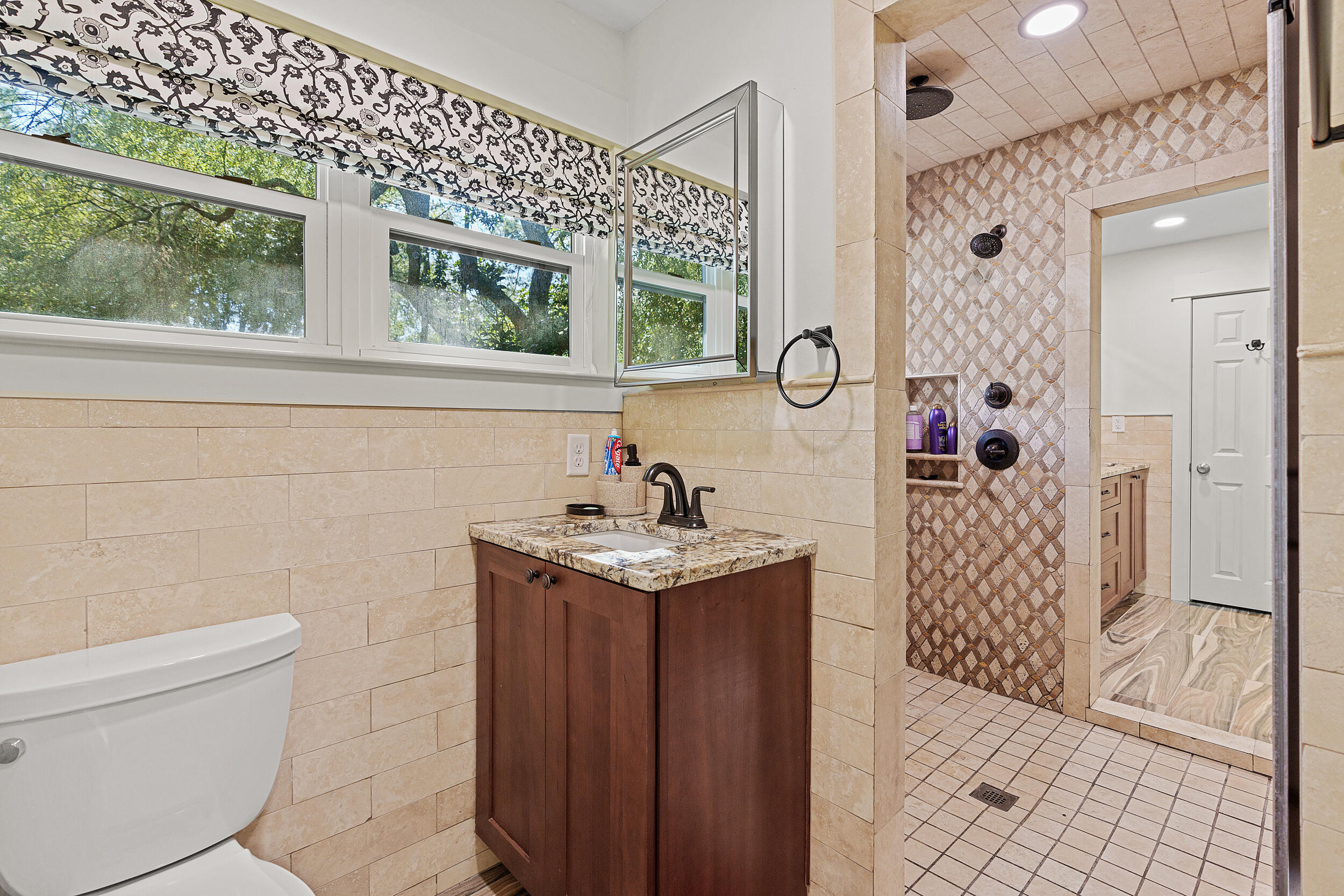 Bathroom with a patterned-tile walk-in shower, dark wood vanity, and wide windows.