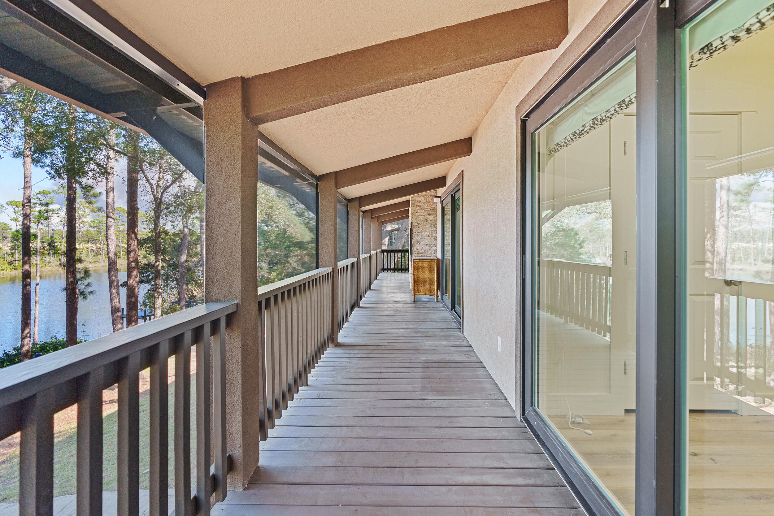 Covered wooden balcony with sliding glass doors overlooking a lake and trees.