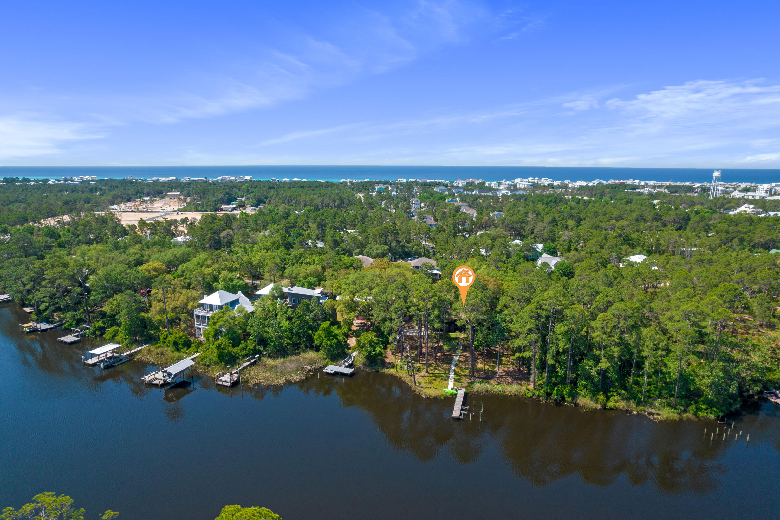 Aerial view of a wooded lakeside property with a dock, neighborhood, and Gulf coastline beyond.