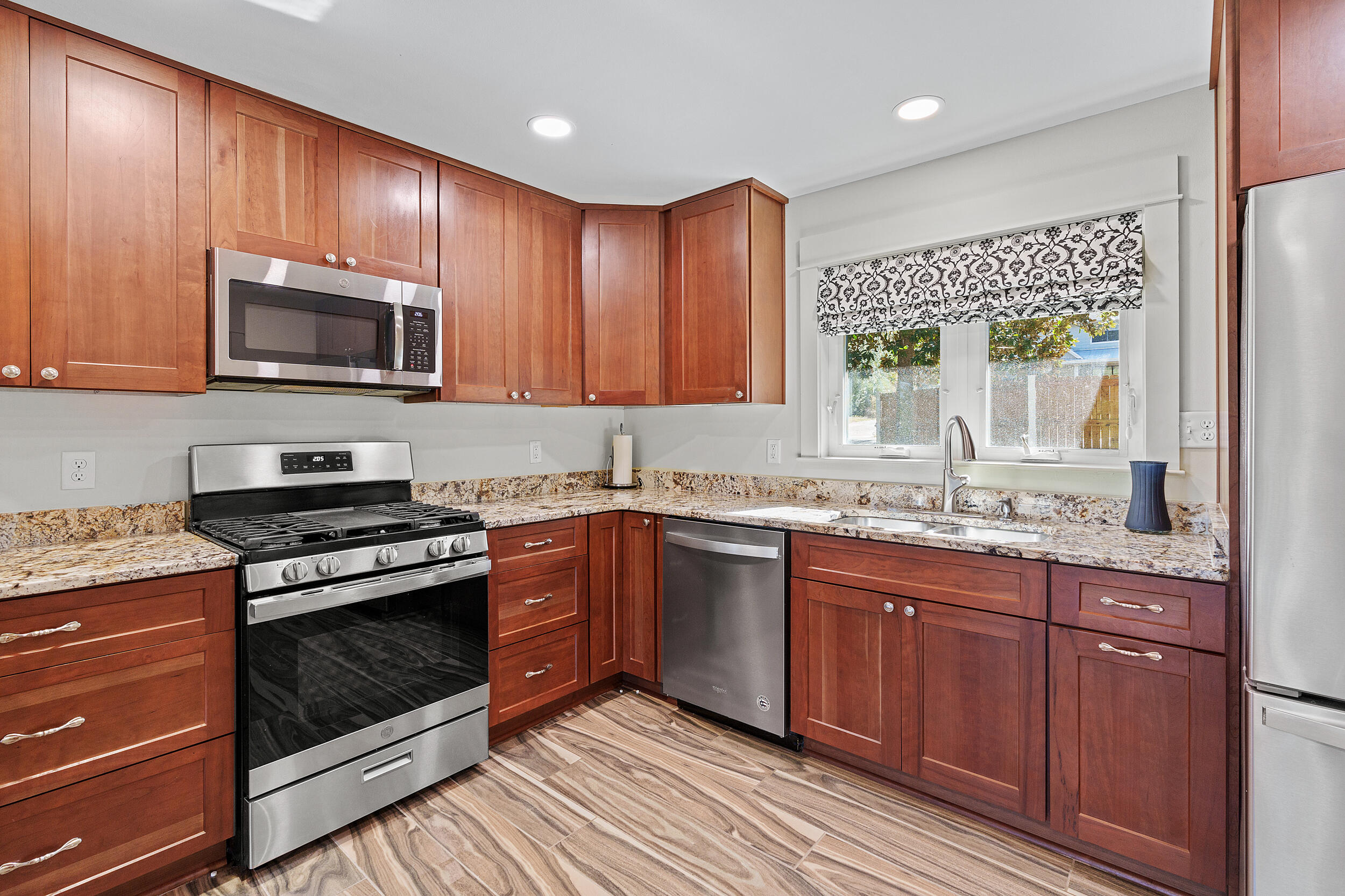 Kitchen with reddish wood cabinets, granite countertops, stainless steel appliances, and a window over the sink.