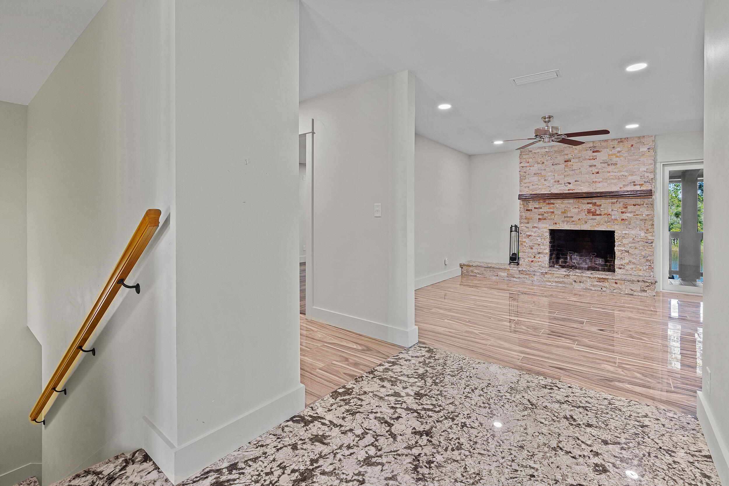 Living room with a stone fireplace, glossy tile floors, and a staircase with a wood handrail.