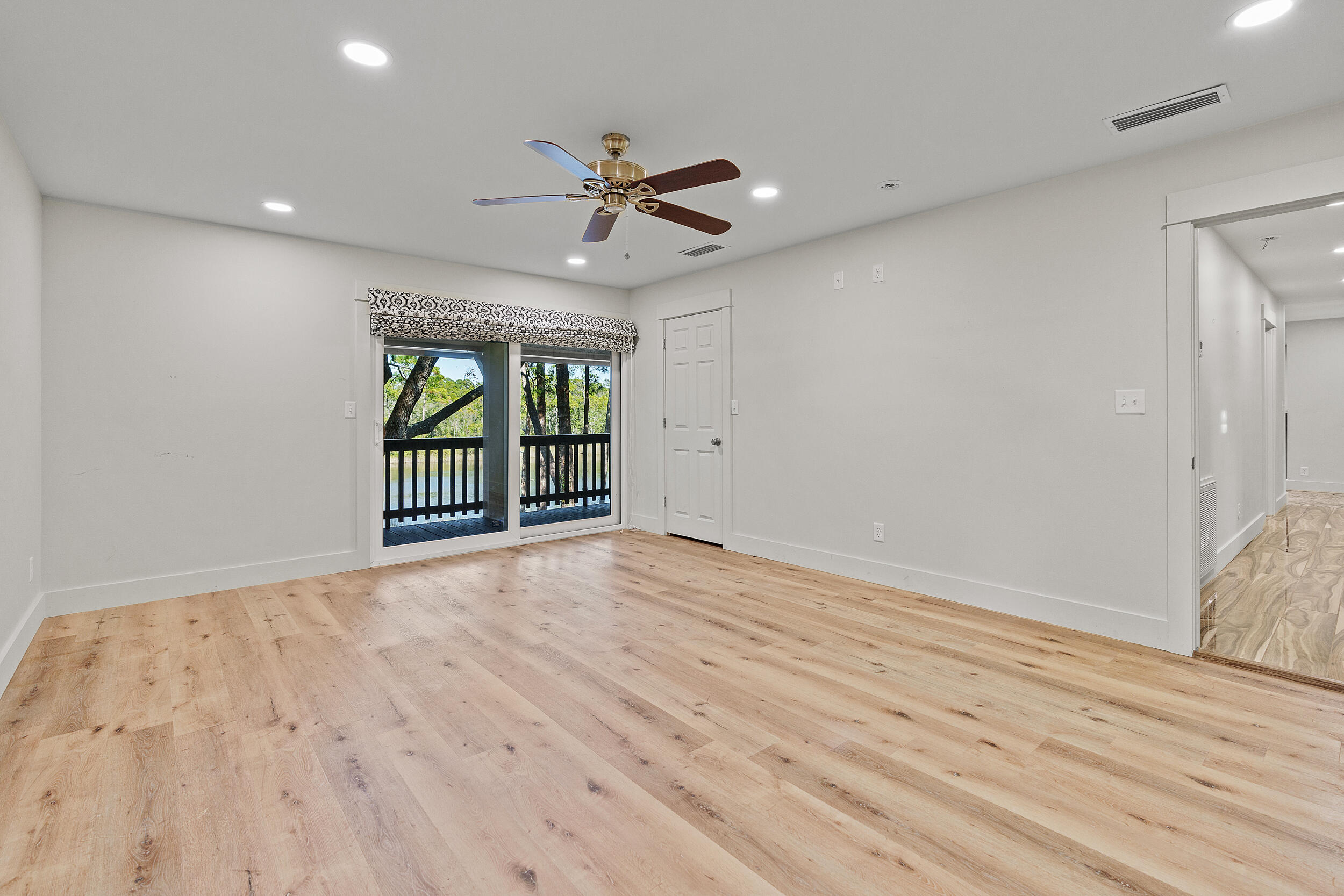 Empty room with pale wood floors and sliding doors overlooking trees and water.