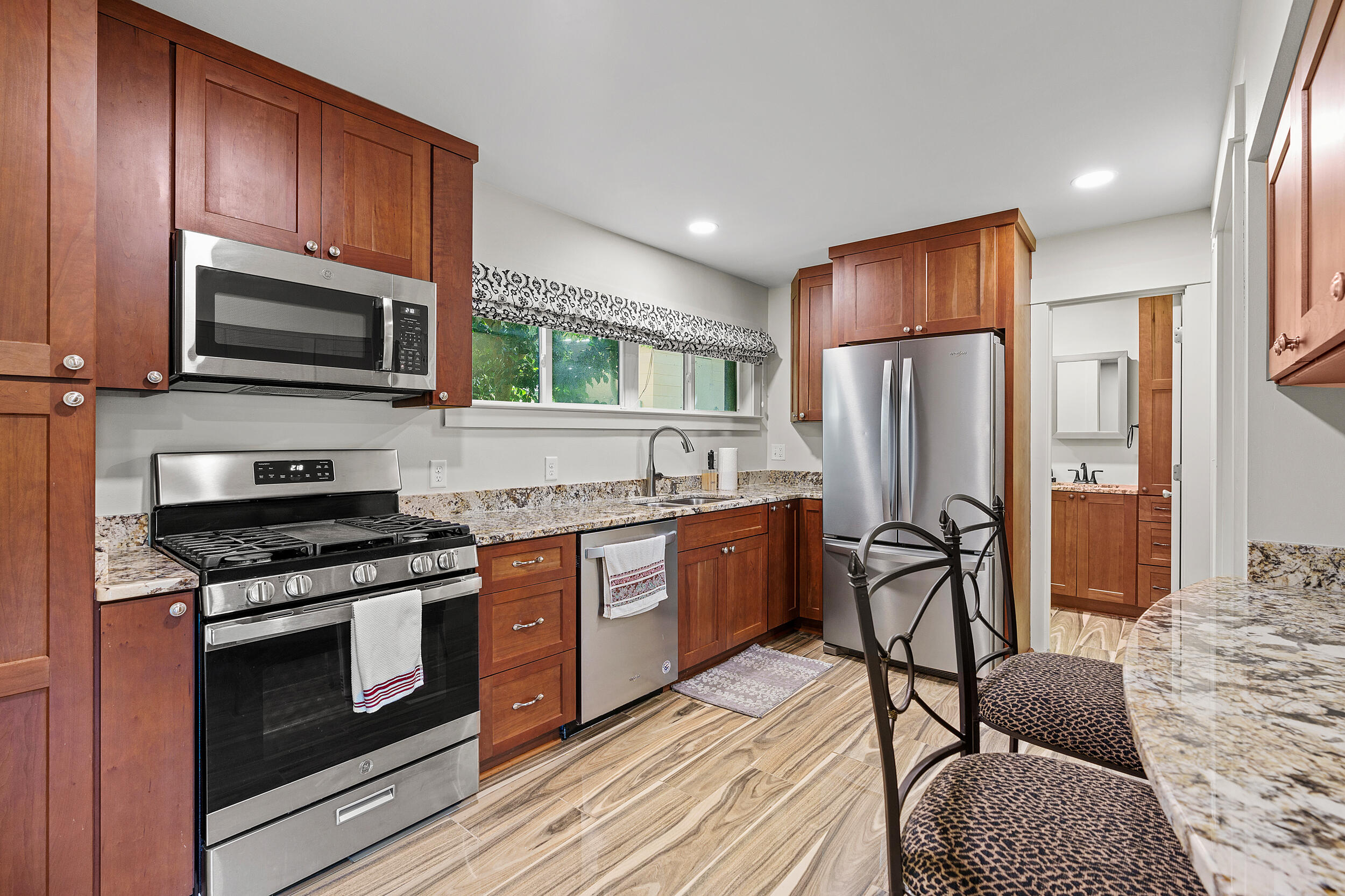 Kitchen with reddish-brown wood cabinets, granite counters, stainless appliances, and a gas range.