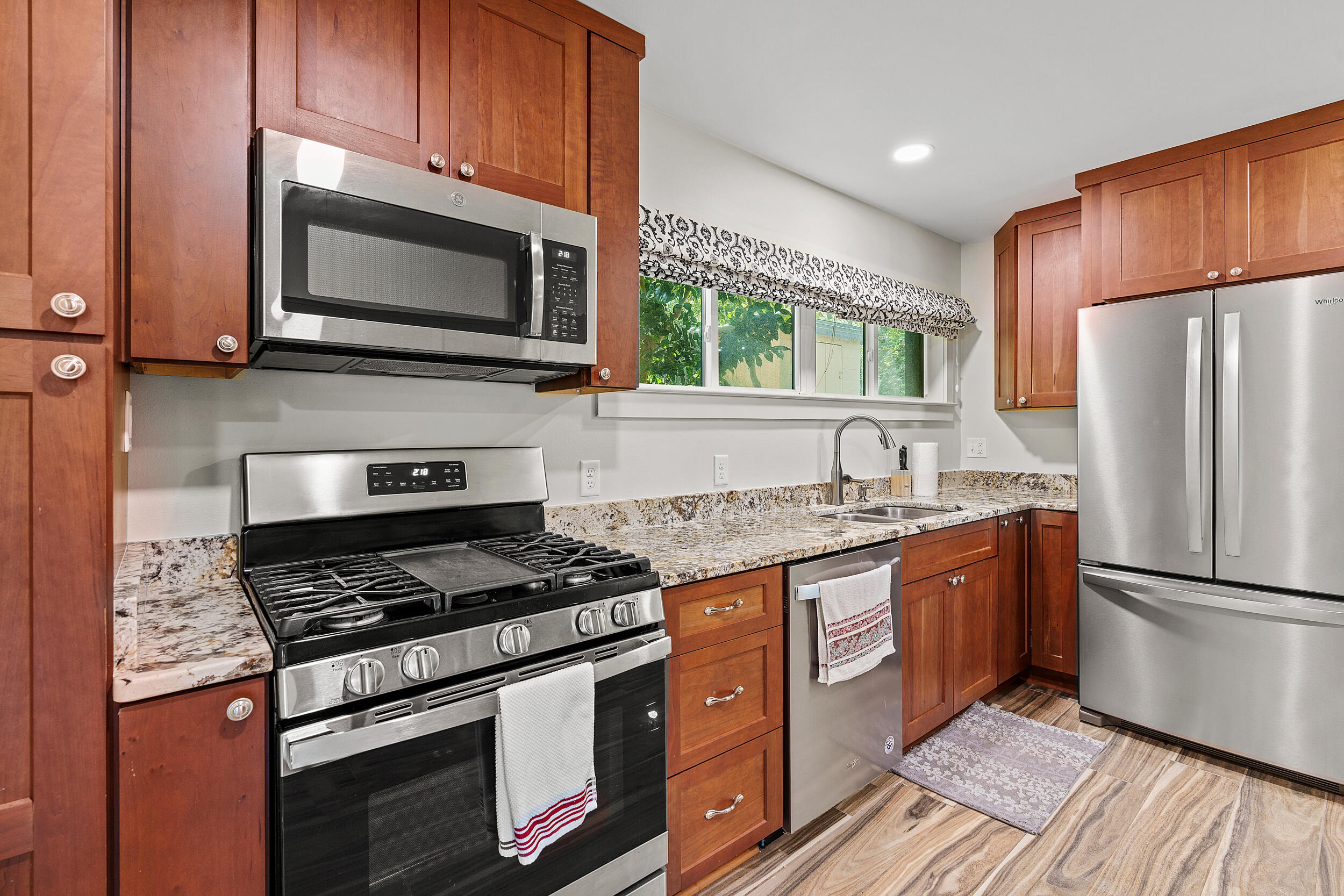 Kitchen with reddish-brown cabinets, granite counters, stainless steel appliances, and a window above the sink.