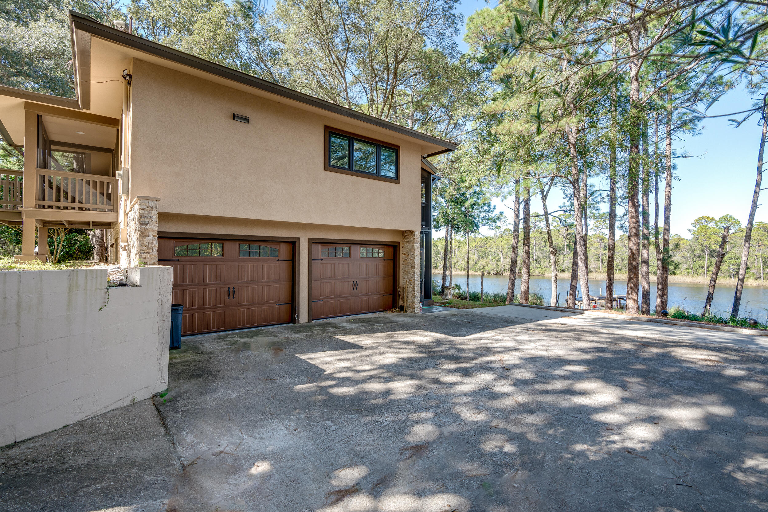 Two-story tan home with a raised balcony and double garage beside a tree-lined lake.