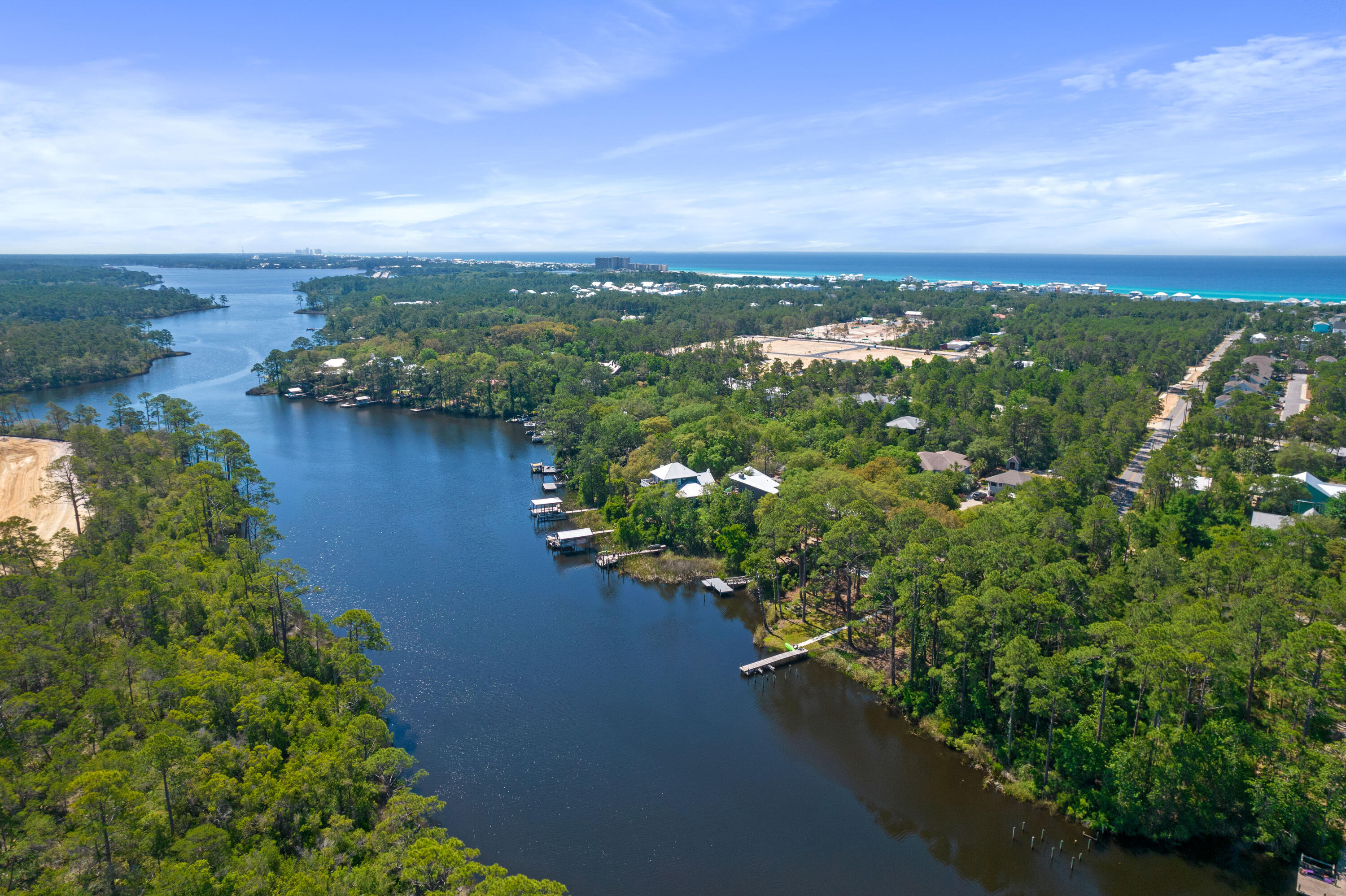 Aerial view of a wooded inlet with waterfront homes and docks, with the sea beyond.