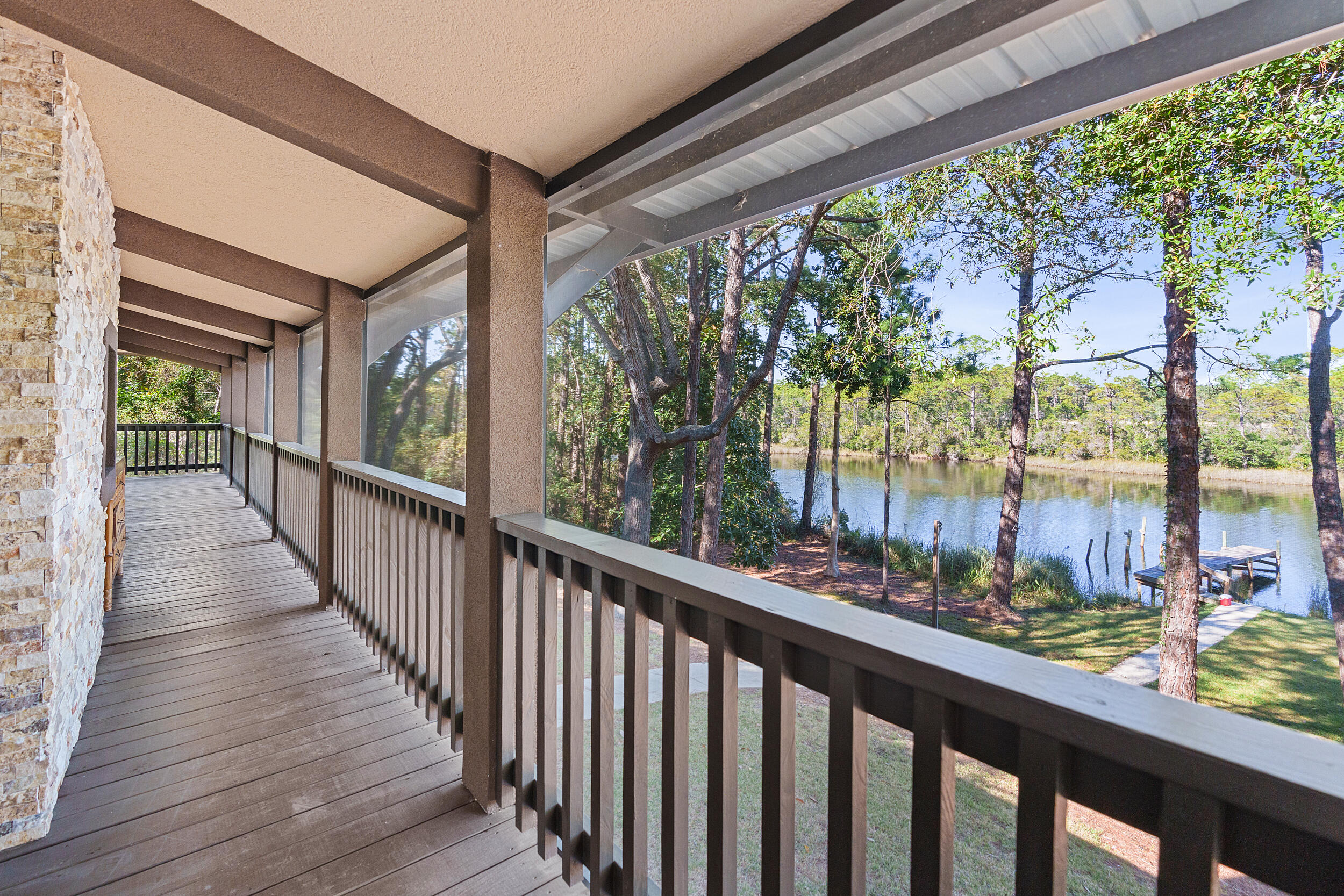 Covered wooden balcony overlooking a tree-lined lake and small dock.