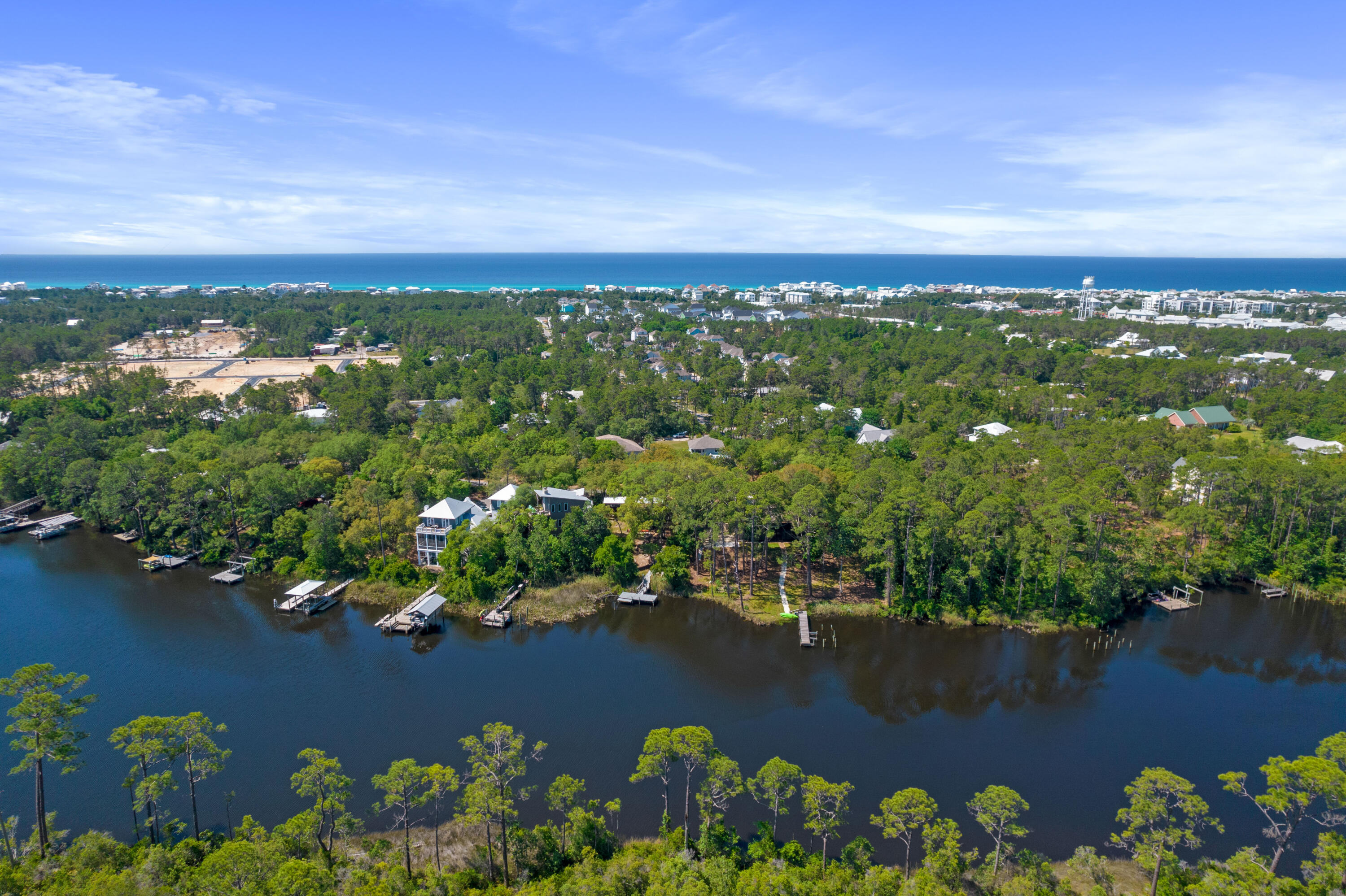 Aerial view of wooded waterfront homes and docks, with a bay and the Gulf beyond.