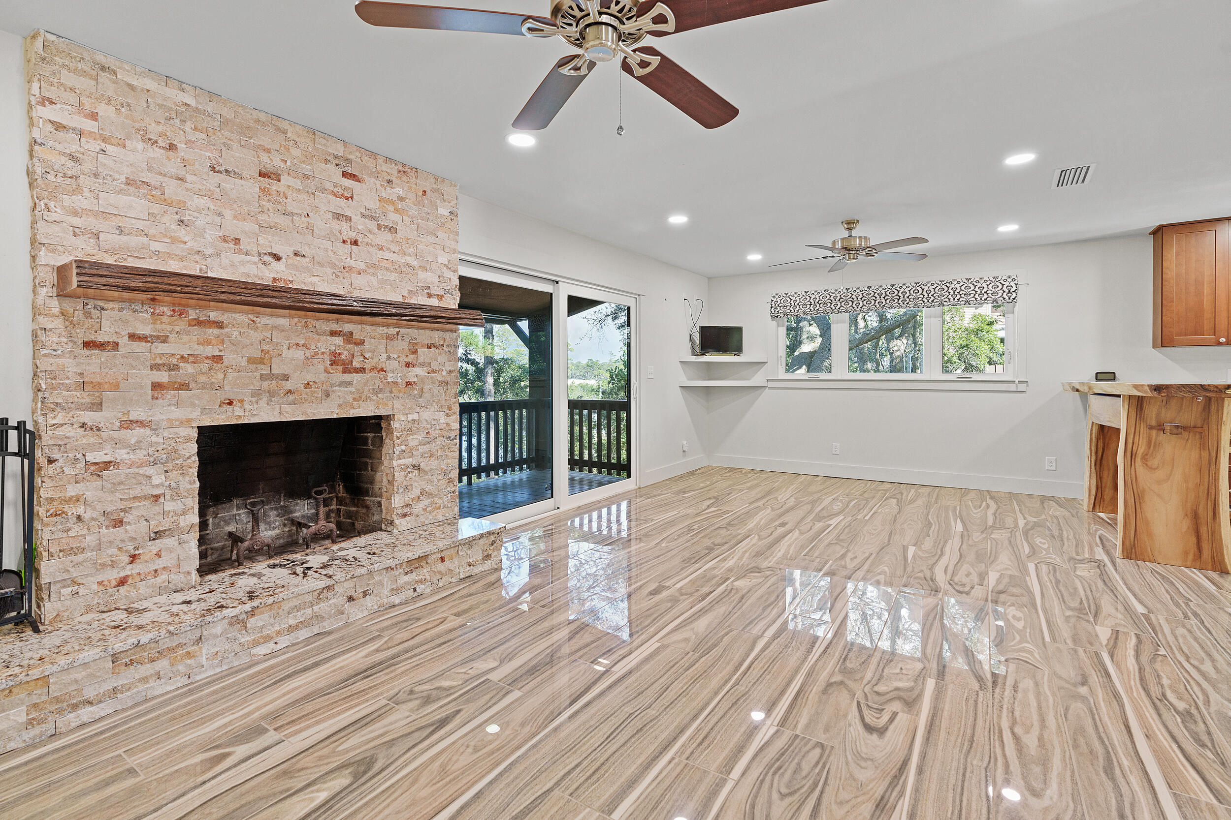 Vacant living room with a stone fireplace, glossy tile floors, and sliding doors opening to a deck.