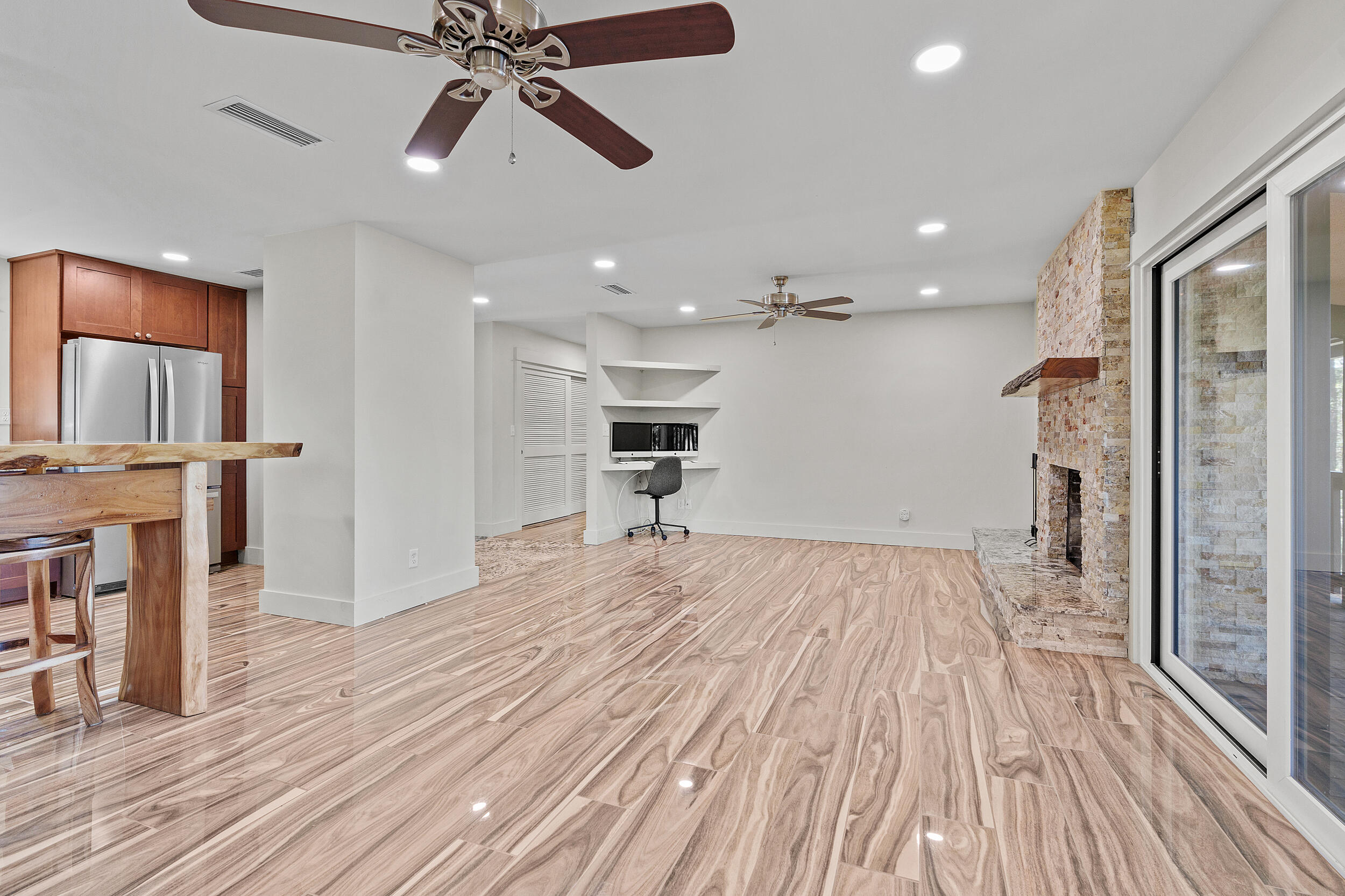 Open living room with a stone fireplace, glossy tile floors, and a built-in desk.