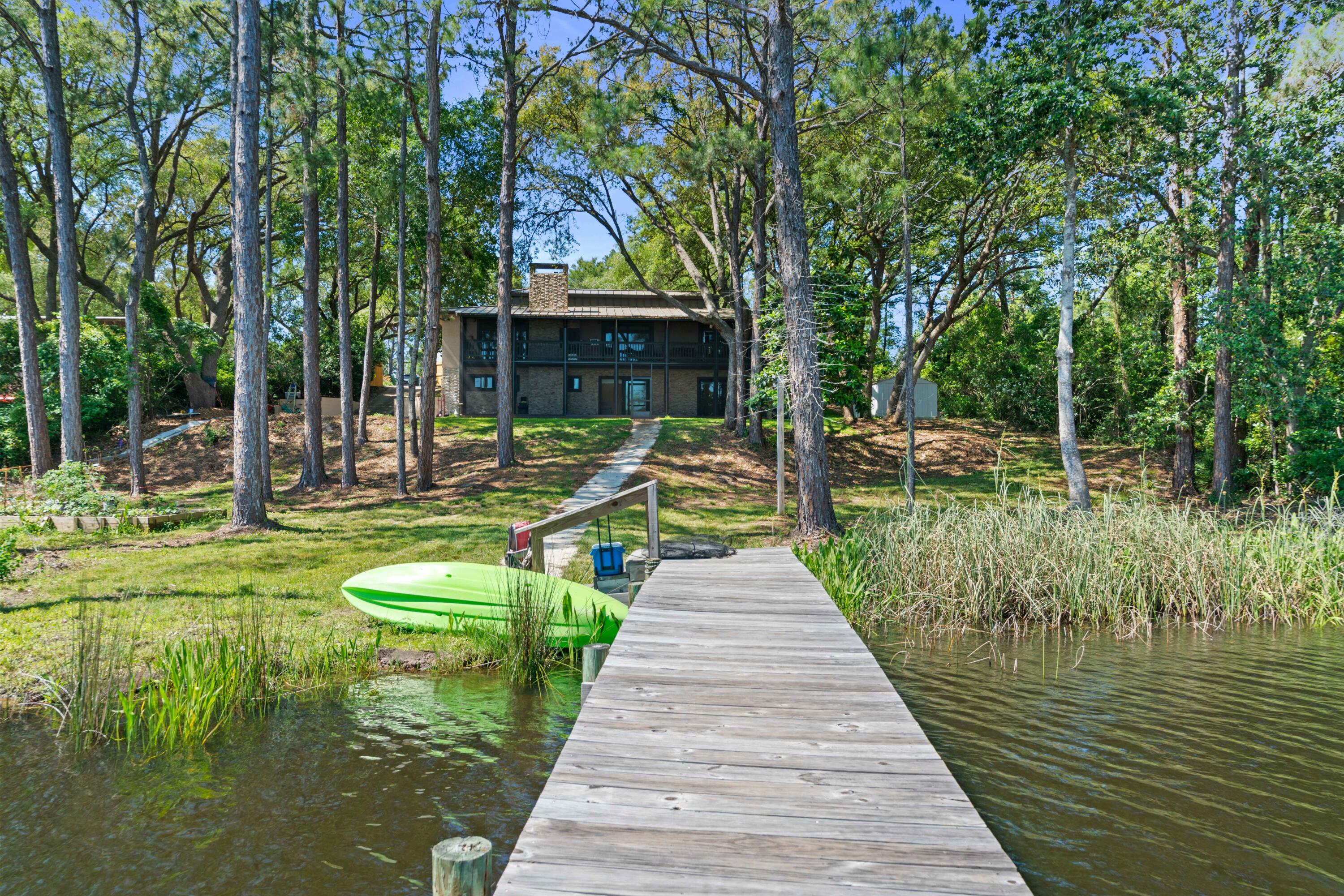 Two-story lakeside house framed by trees, viewed from a dock beside a bright green kayak.