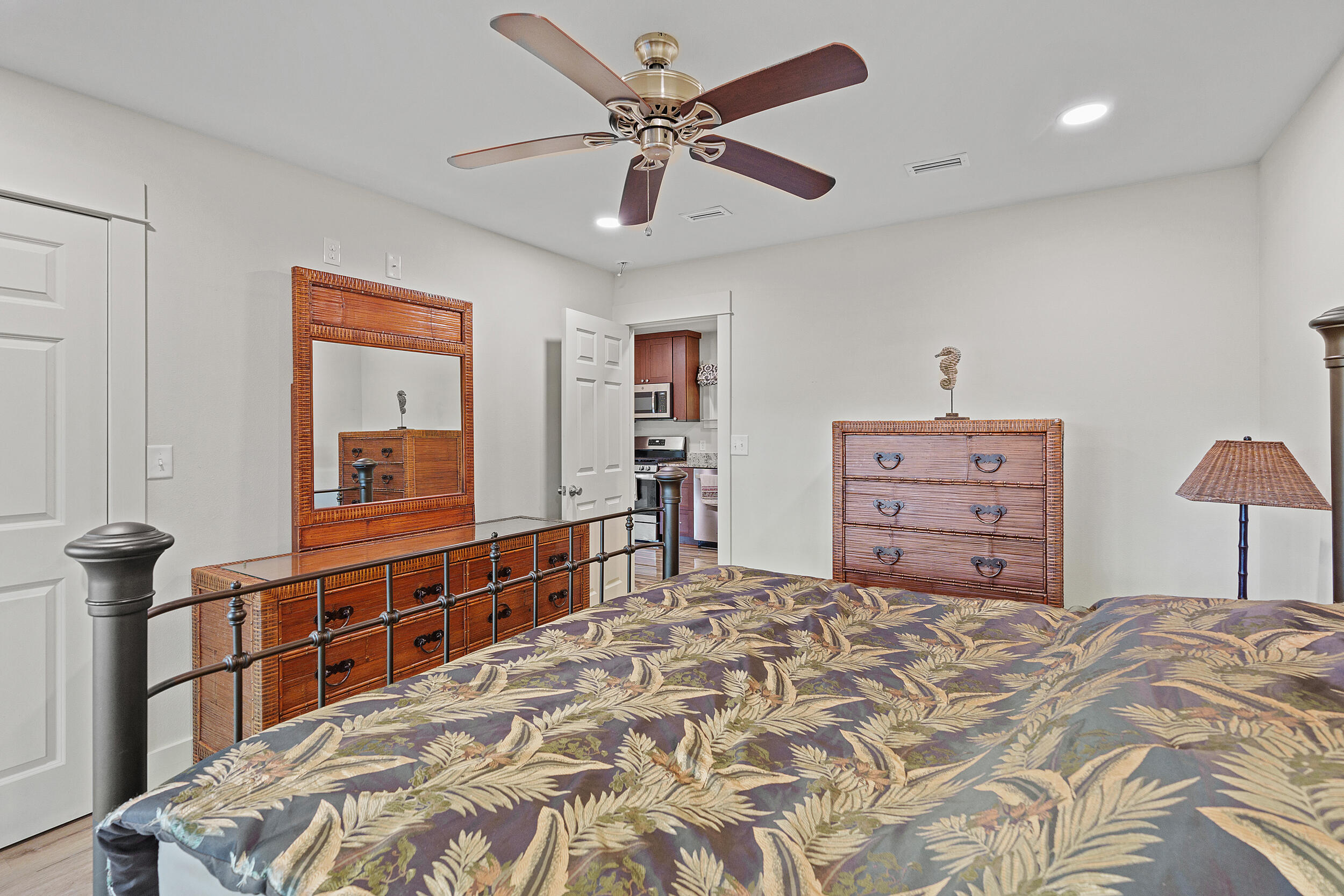 Furnished bedroom with tropical leaf bedding, rattan-style dressers, and a ceiling fan.
