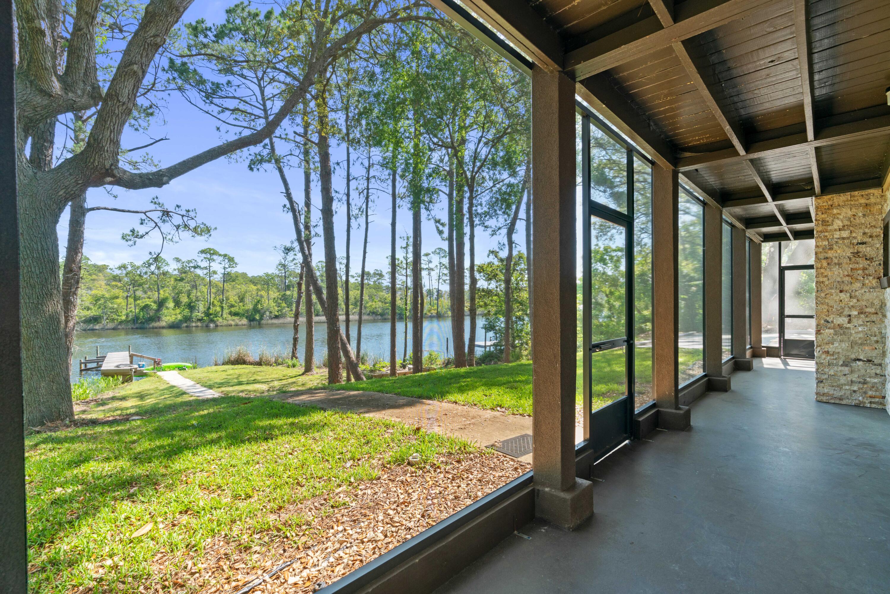 Covered waterfront porch overlooking a wooded riverbank, lawn, and small dock.