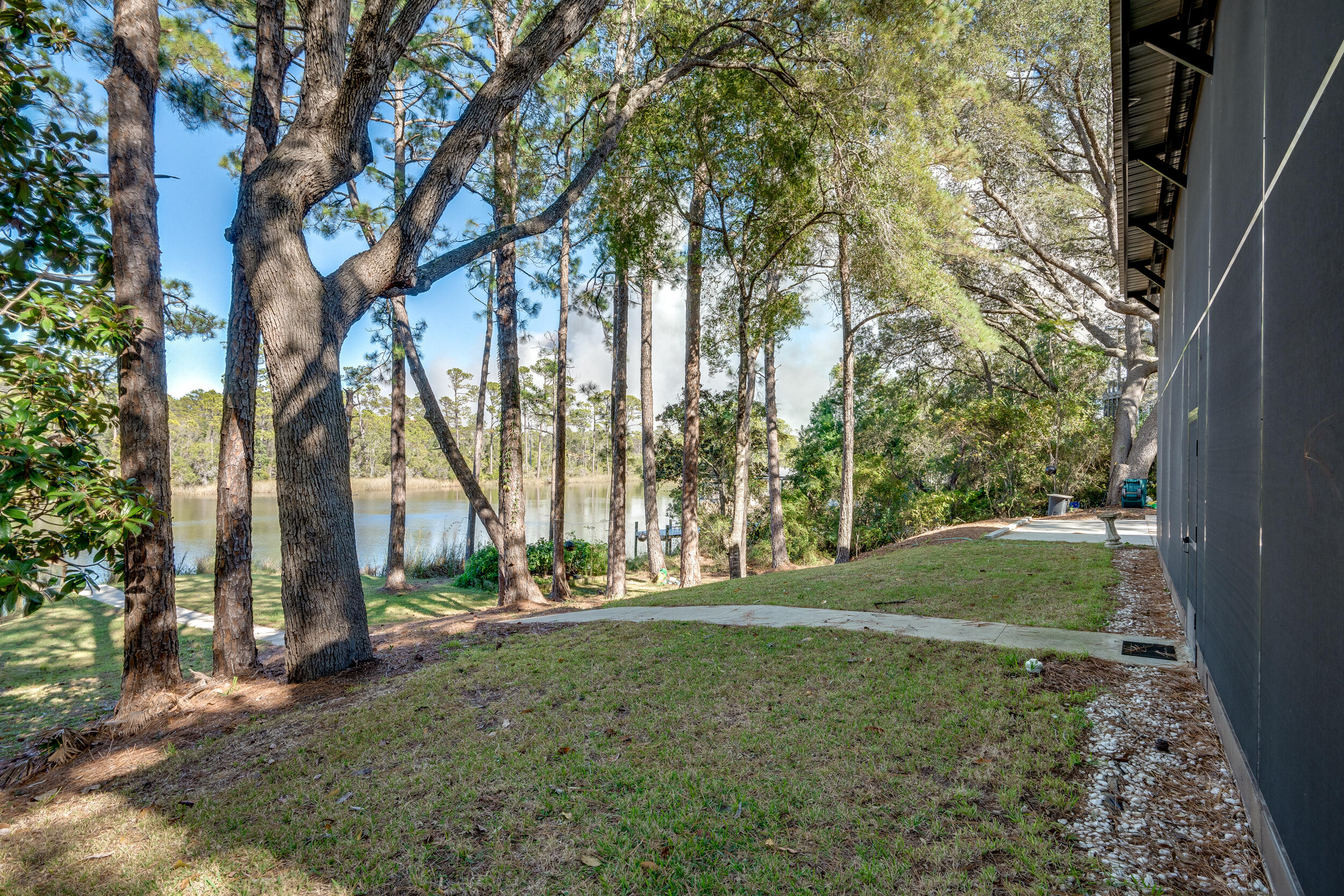 Tree-lined lakeside yard beside a home, with a lawn and concrete walkway.