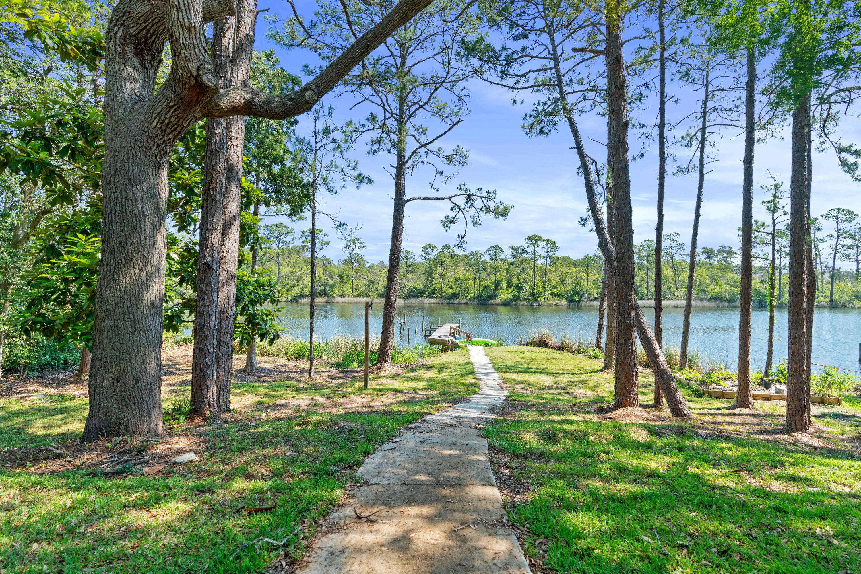 A concrete path crosses a tree-shaded lawn to a small dock on a calm river.
