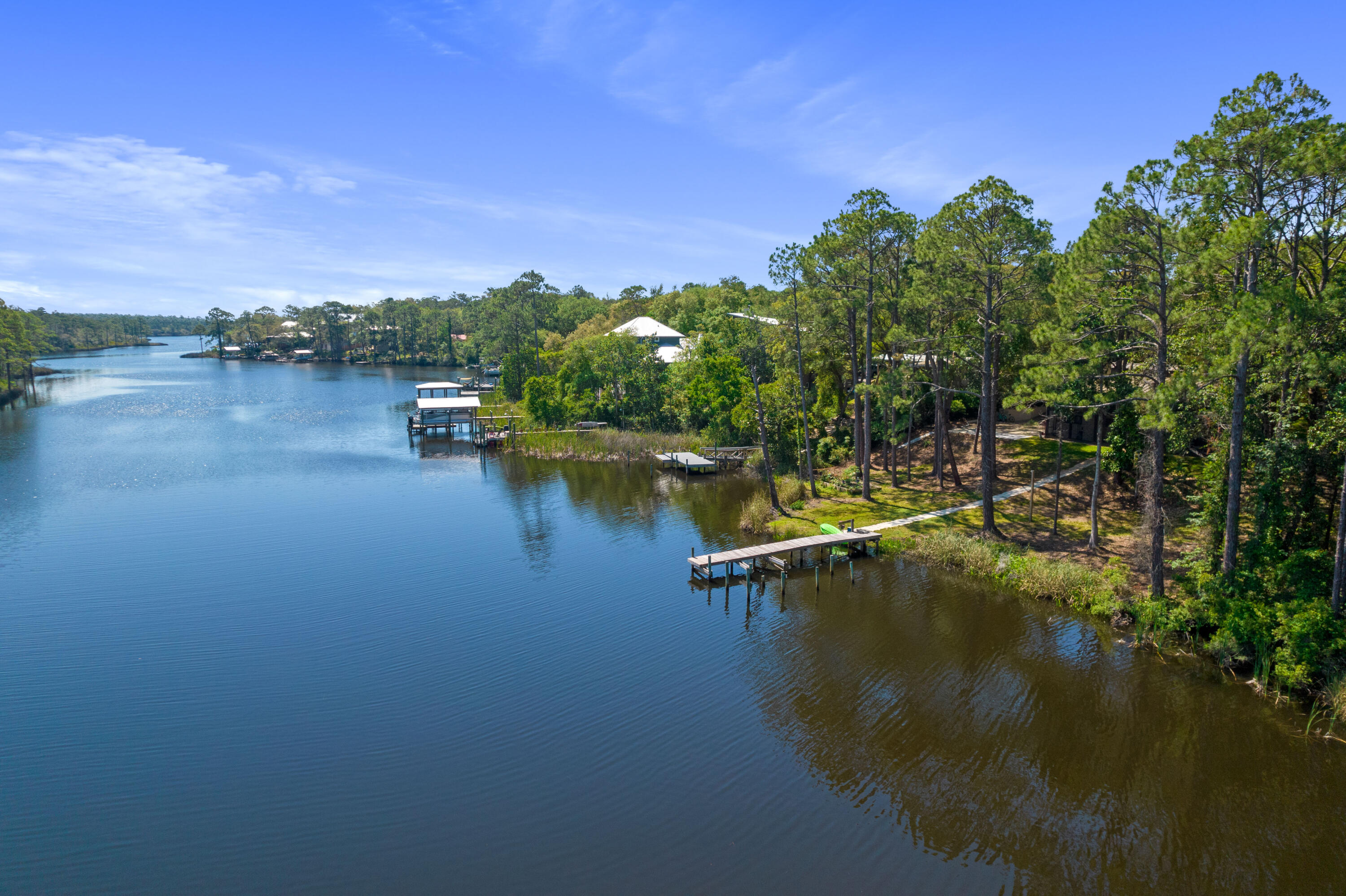 Aerial view of wooded waterfront property with a long dock along a calm inlet.