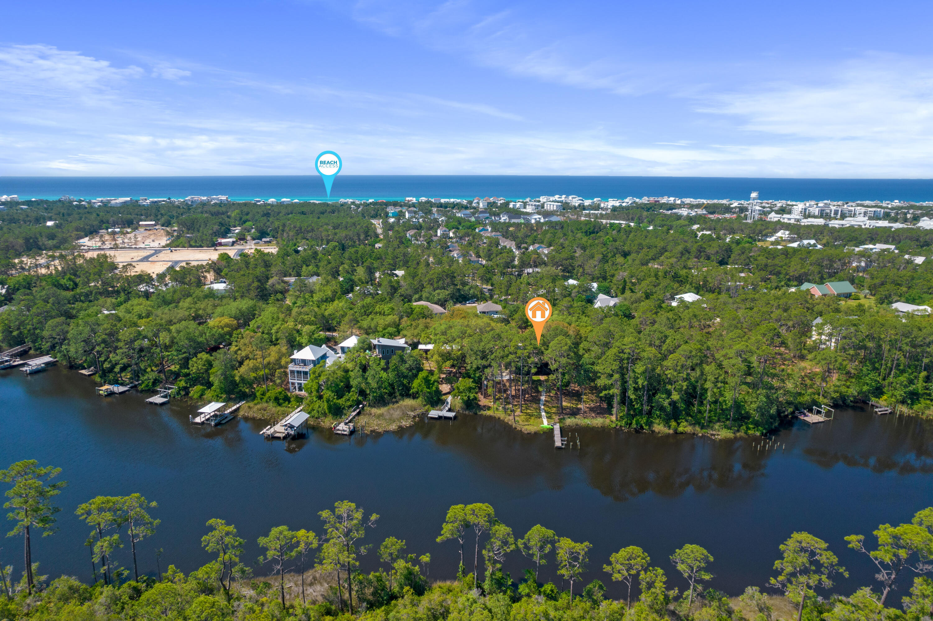 Aerial view of a wooded waterfront property between an inlet and the ocean, with home and beach access markers.