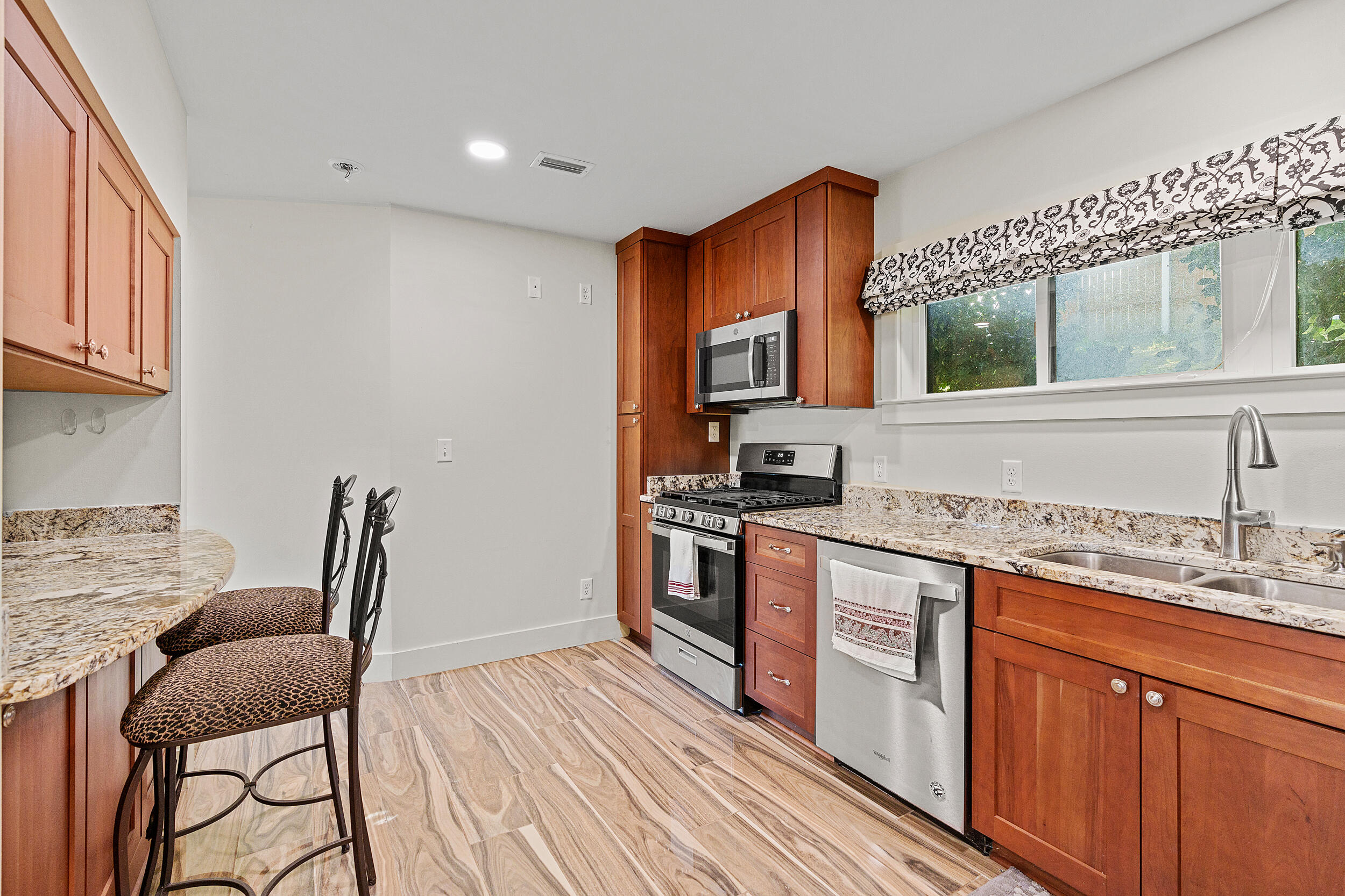 Kitchen with reddish wood cabinets, granite counters, stainless steel appliances, and two bar stools.